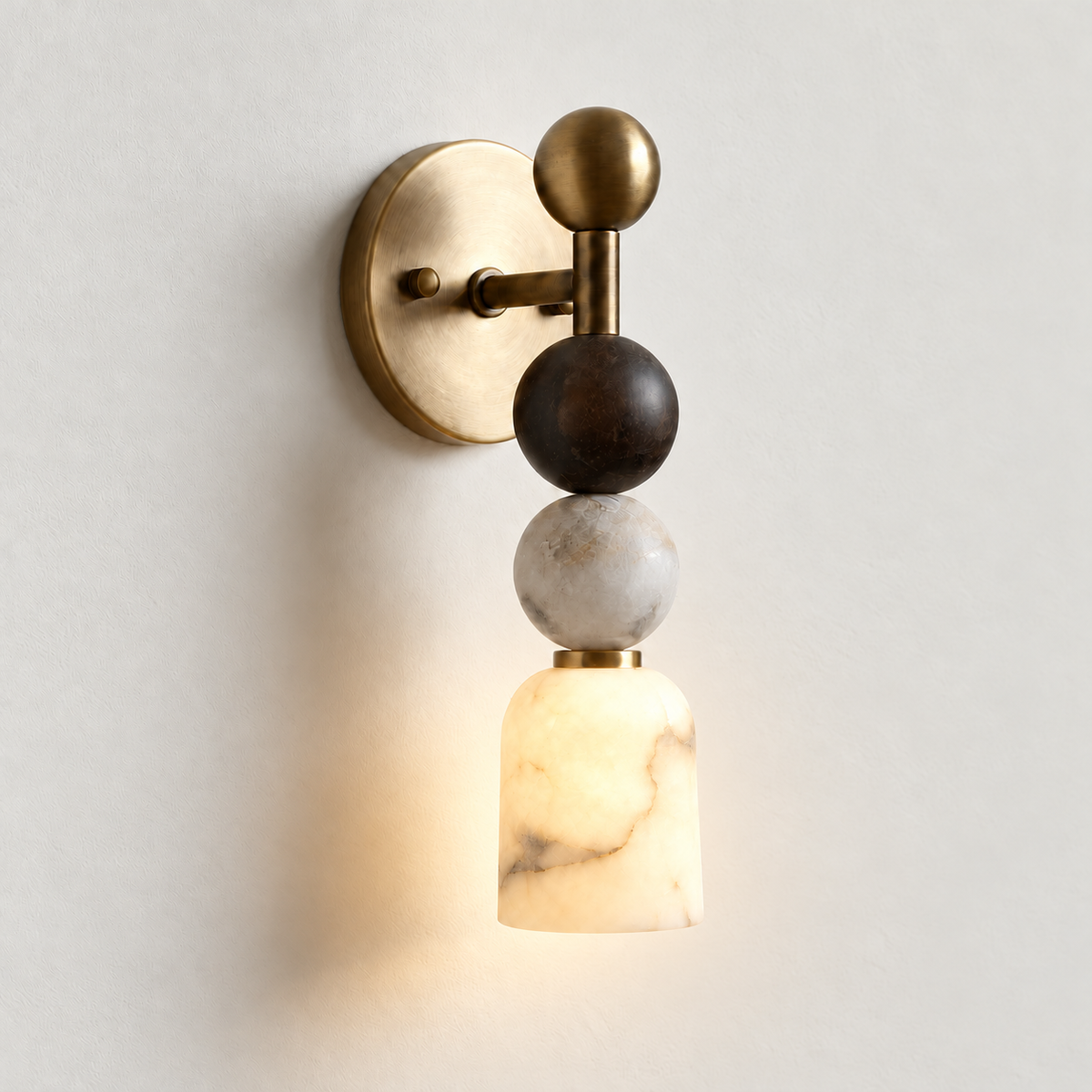Alabaster and brass wall sconce with its lower bell illuminated on warm ivory.