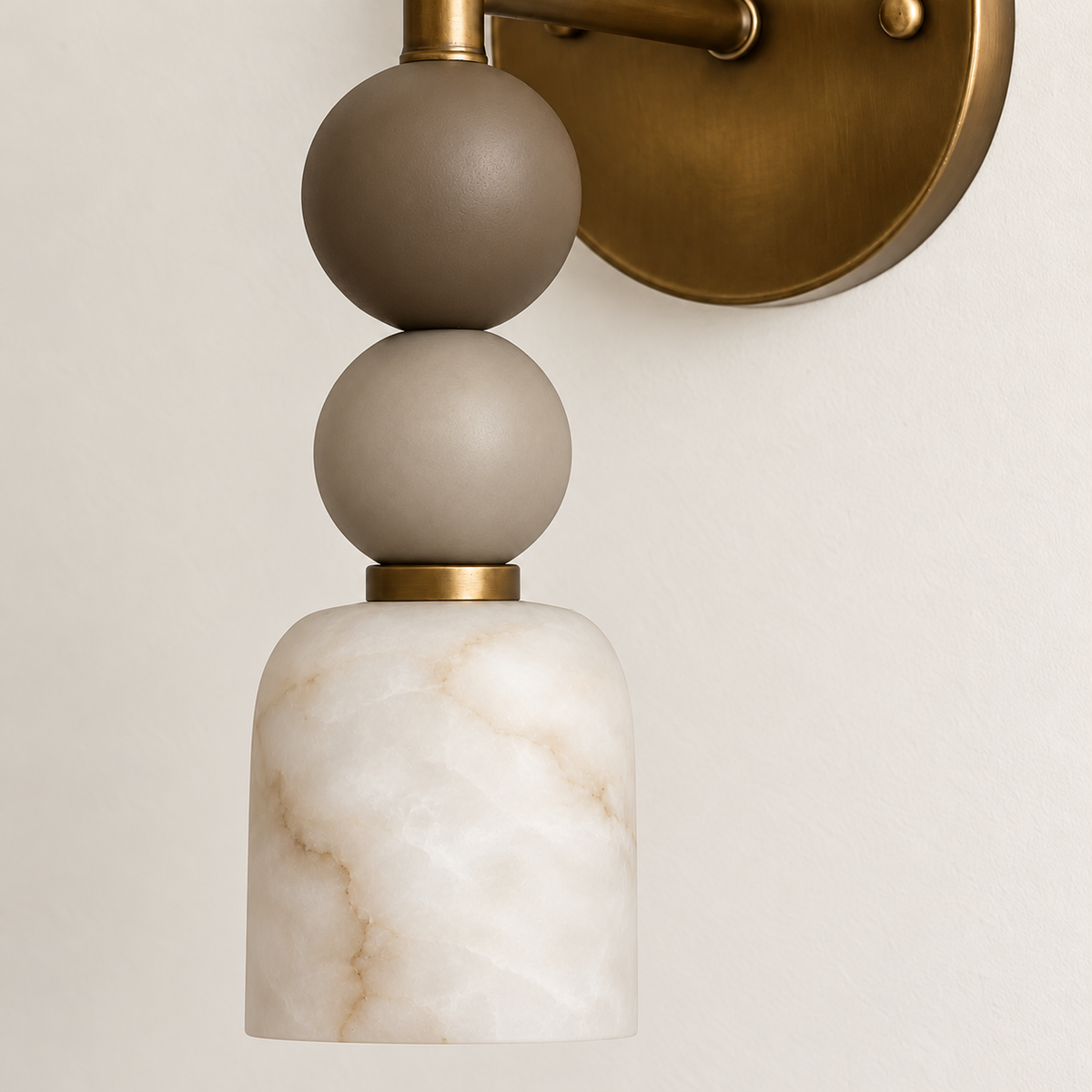 Angled view of alabaster and brass wall sconce with stacked spheres.
