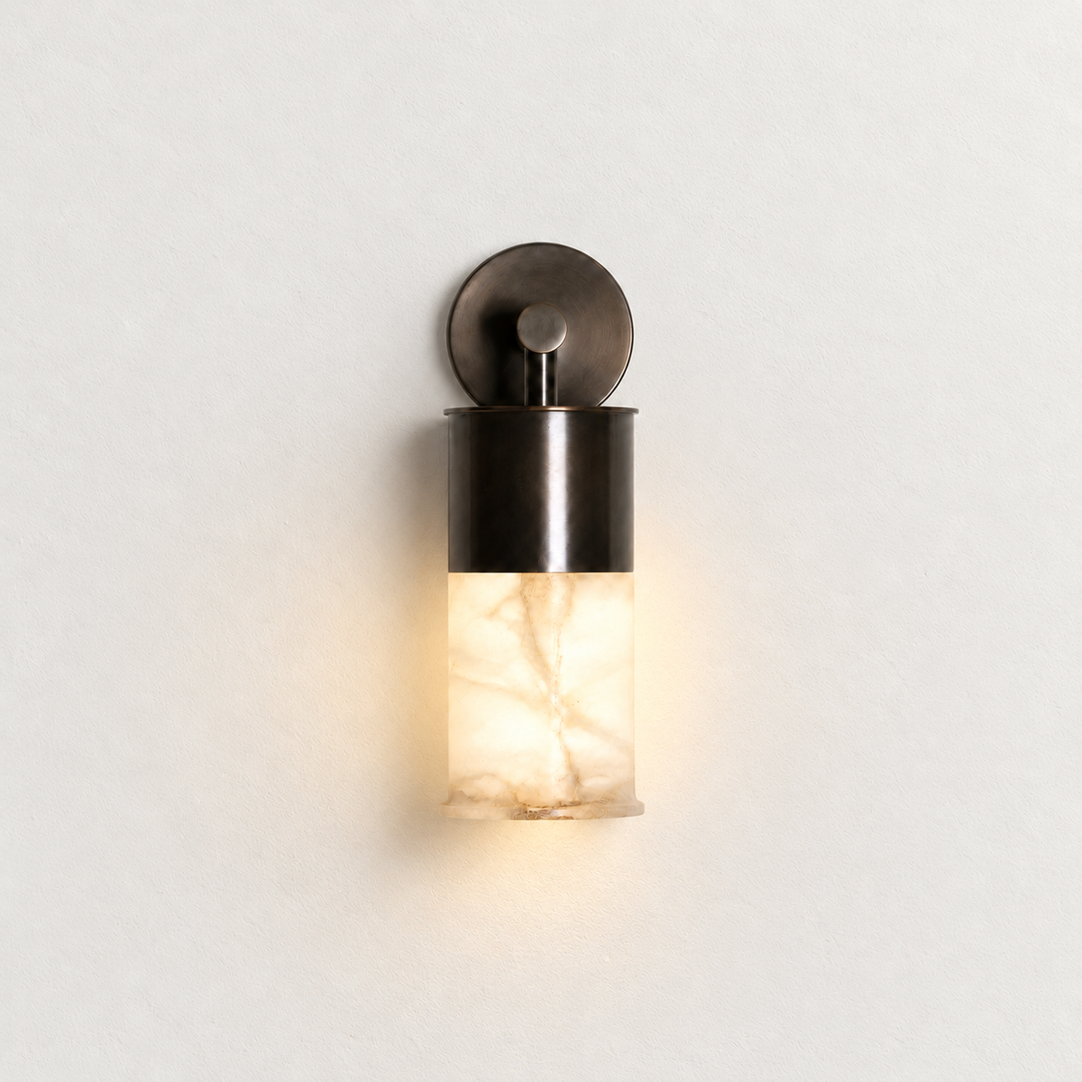 Alabaster cylinder wall sconce mounted on ivory plaster, illuminated.