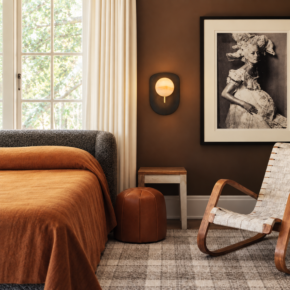 Alabaster and patinated brass shield sconce beside a bed in a brown bedroom.