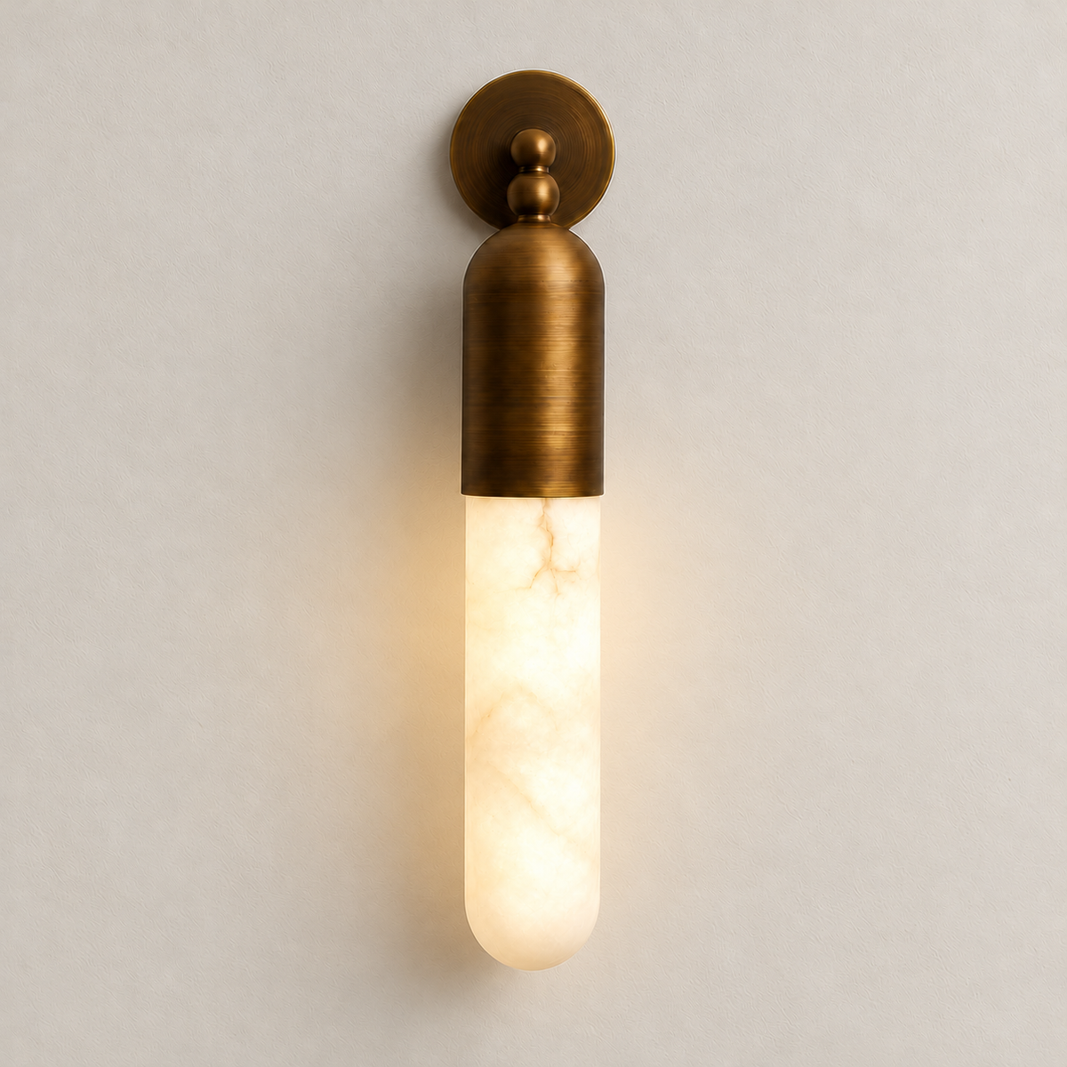 Brass and alabaster tube wall sconce glowing on the same ivory background.