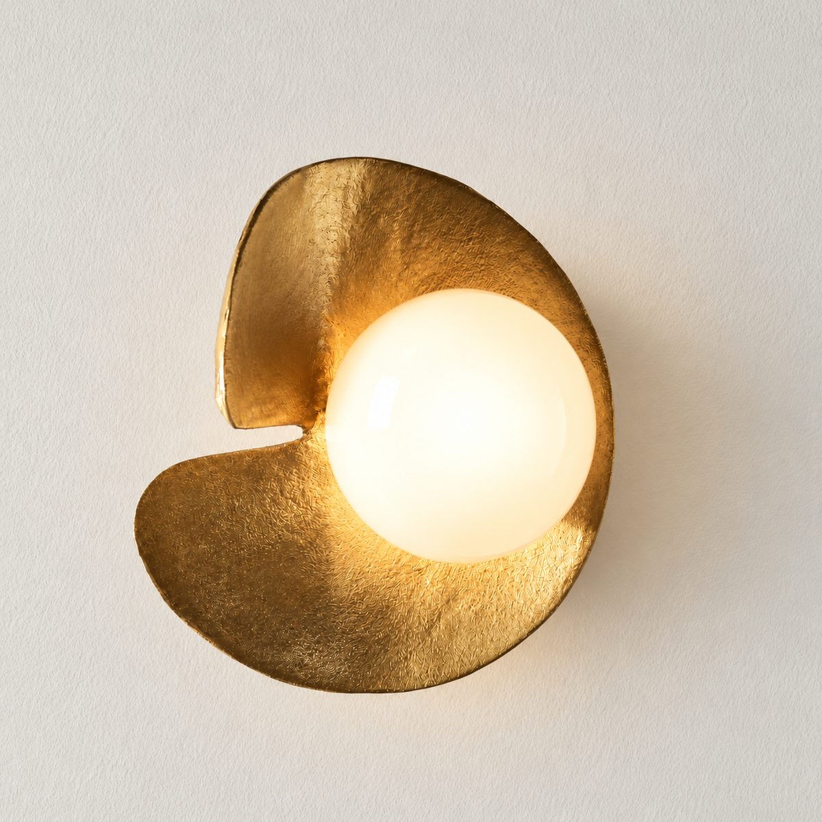 The same Aulia brass sconce with its glass globe illuminated.