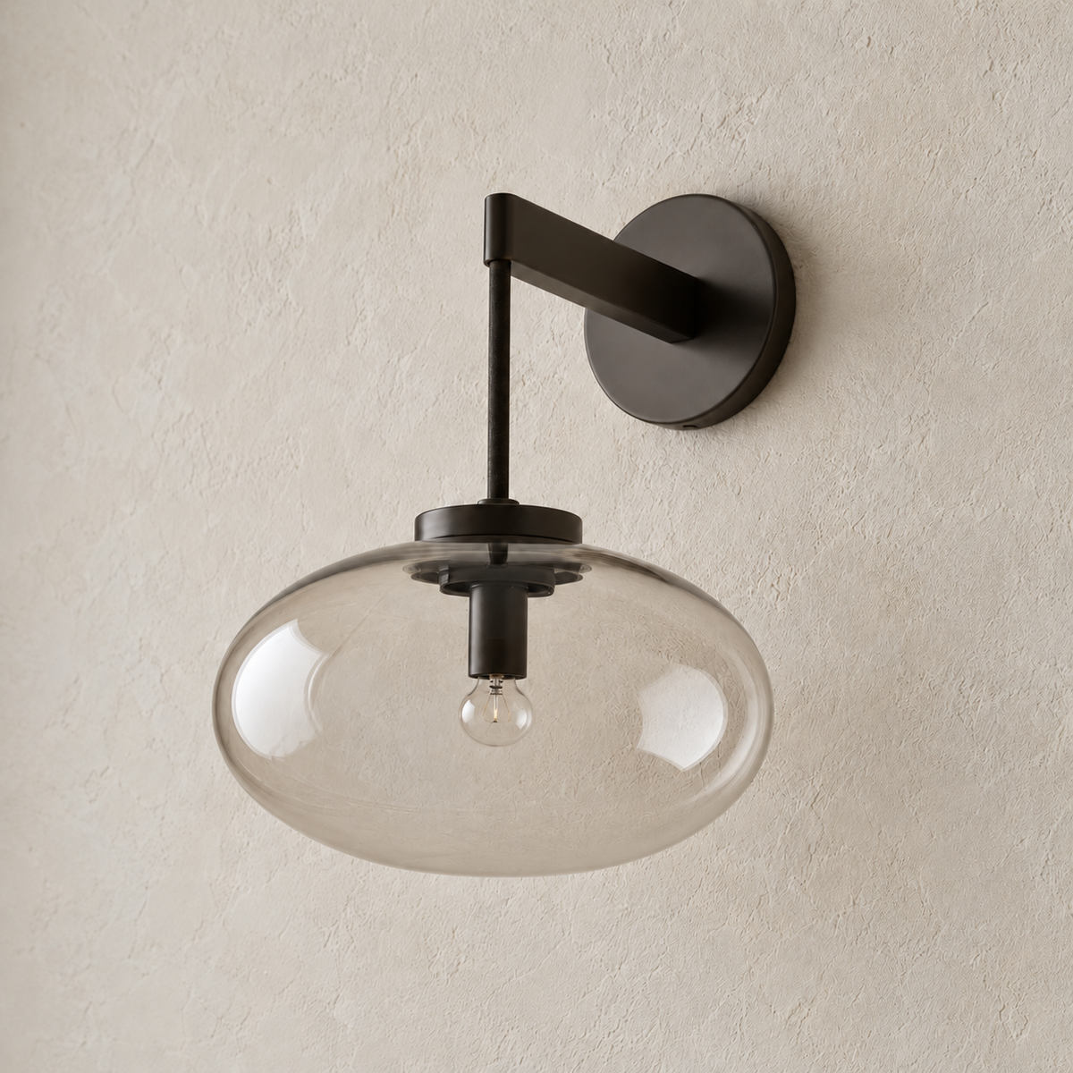 Black wall sconce with a lightly smoky glass shade, switched off on ivory plaster.