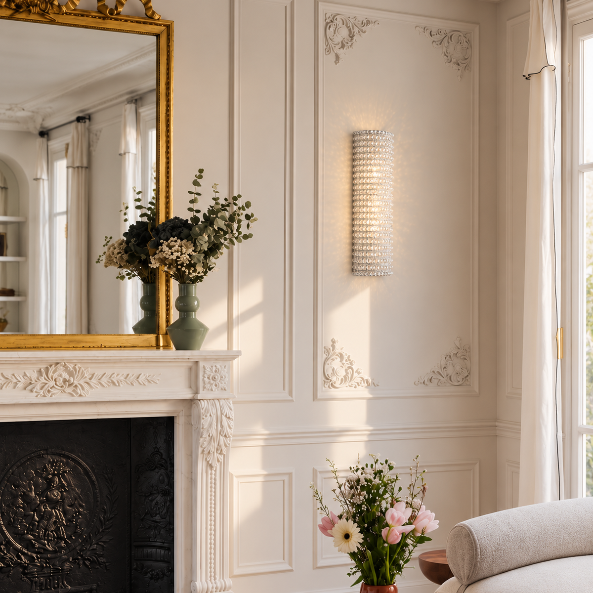 Short clear crystal wall sconce beside a gilt mirror and cream Parisian fireplace.