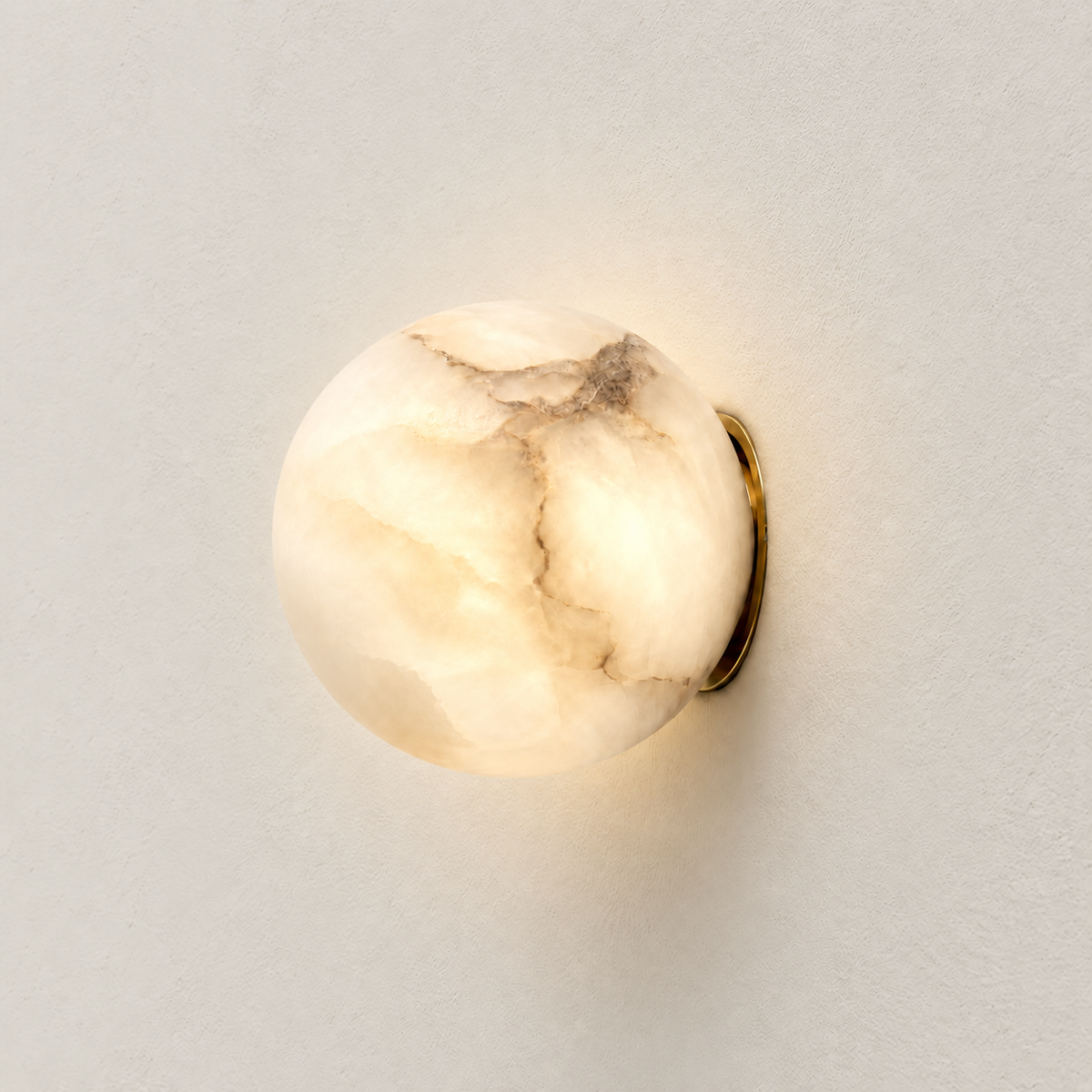 Alabaster globe wall sconce illuminated with warm light, showing natural stone veining and a brass backplate.