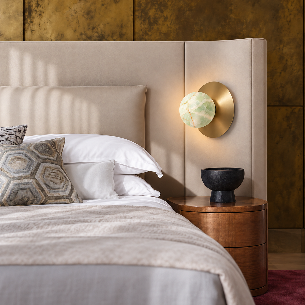 Green onyx globe and brass disc sconce mounted beside an upholstered headboard.
