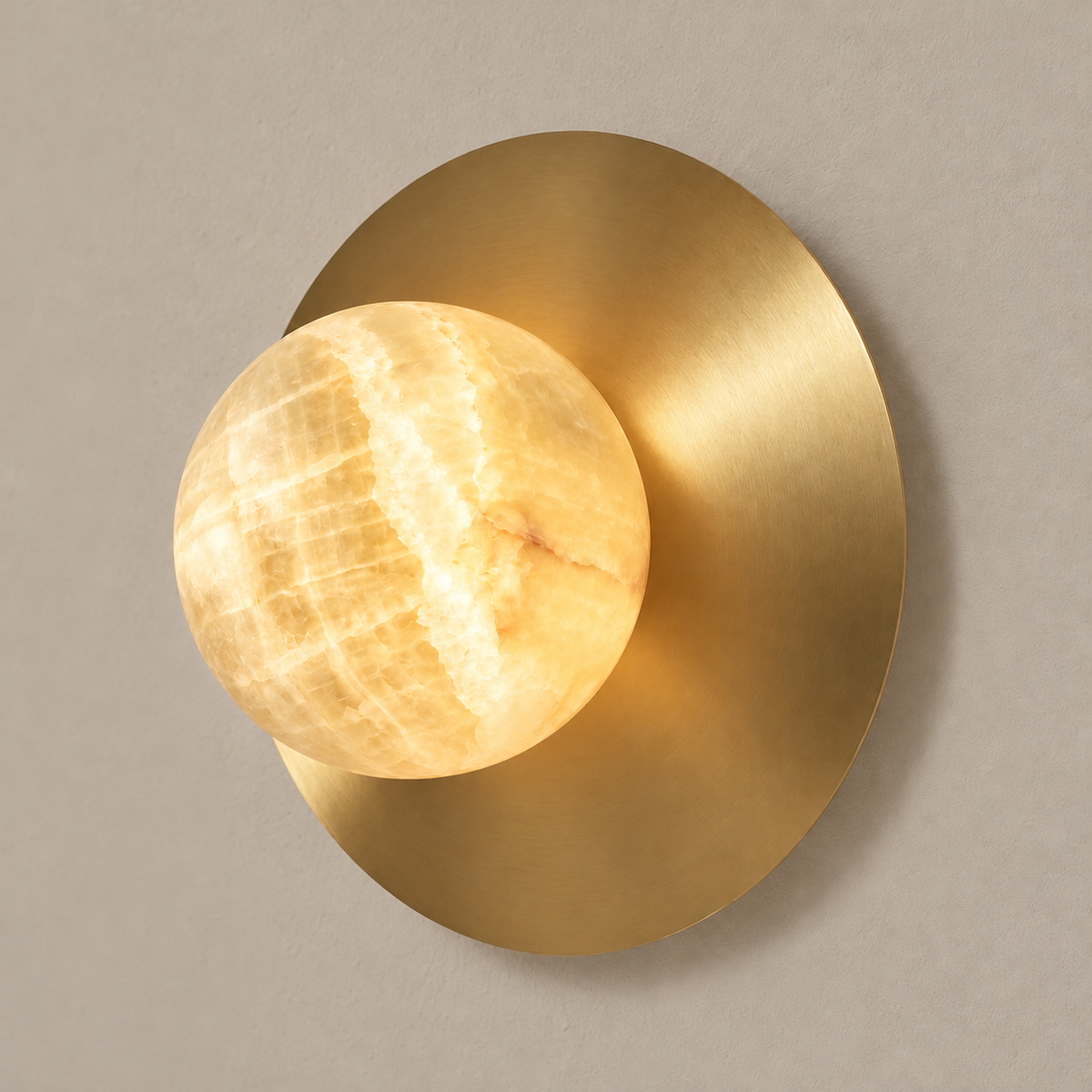Honey onyx globe sconce illuminated against its brass disc.