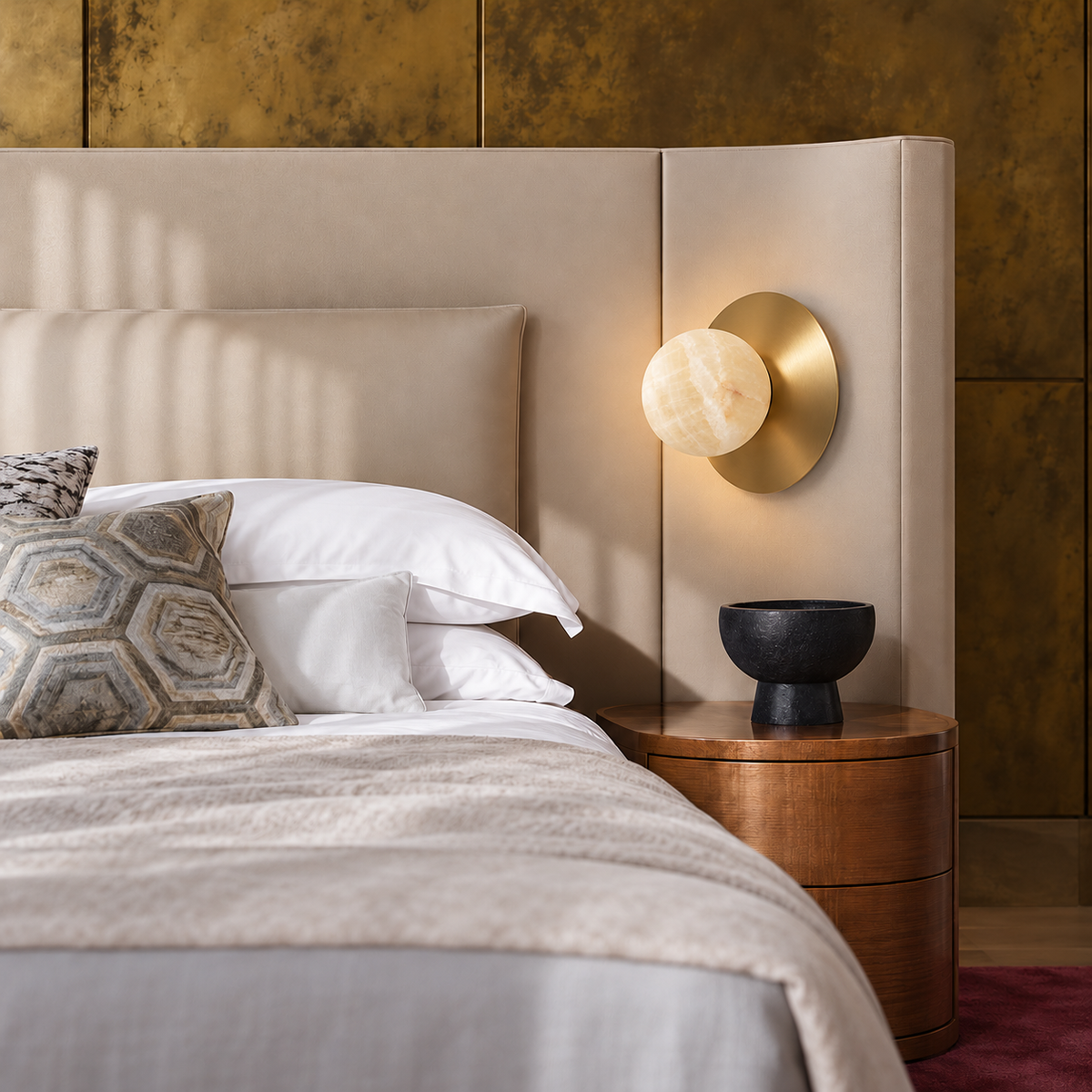 Honey onyx globe and brass disc sconce mounted beside an upholstered headboard.