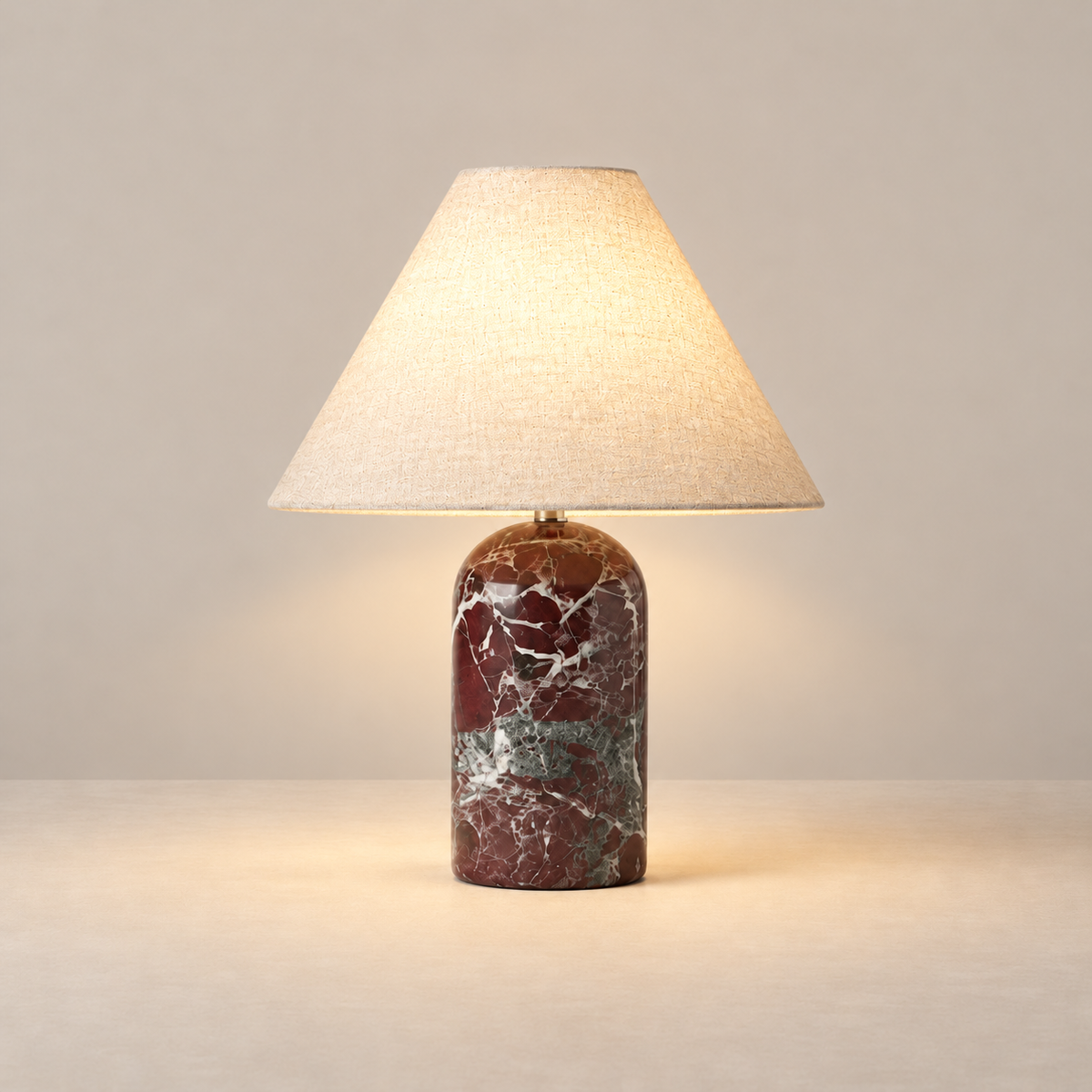 Red marble table lamp with its linen shade illuminated.