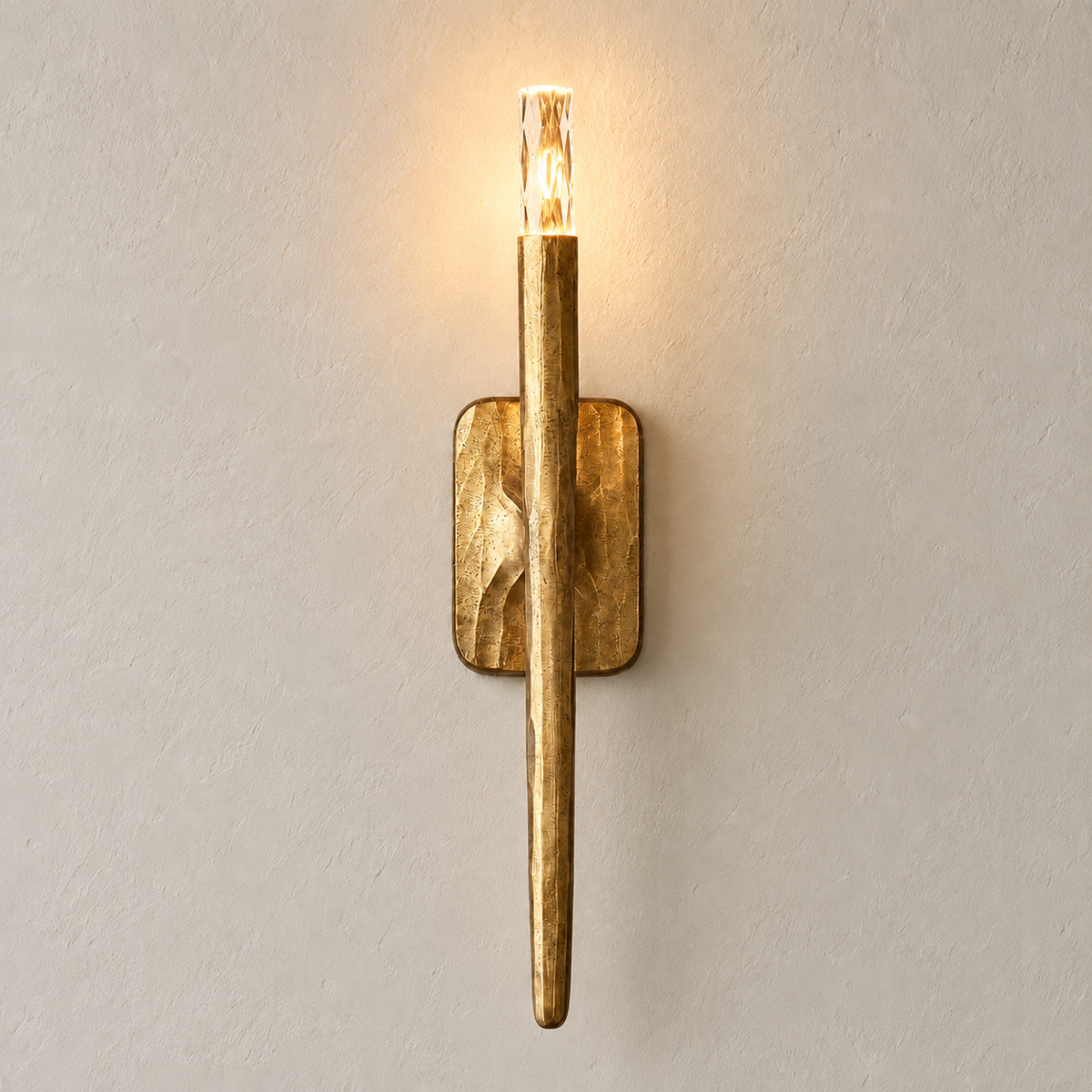 Front view of the sculptural brass wall sconce with a clear crystal tip, illuminated.