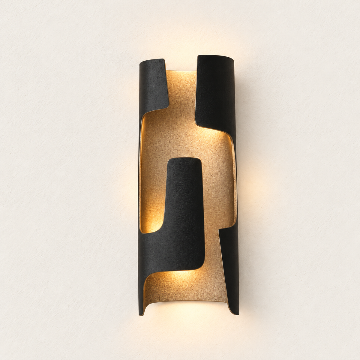 Slender dark patinated bronze folded sconce illuminated against the same warm ivory backdrop.