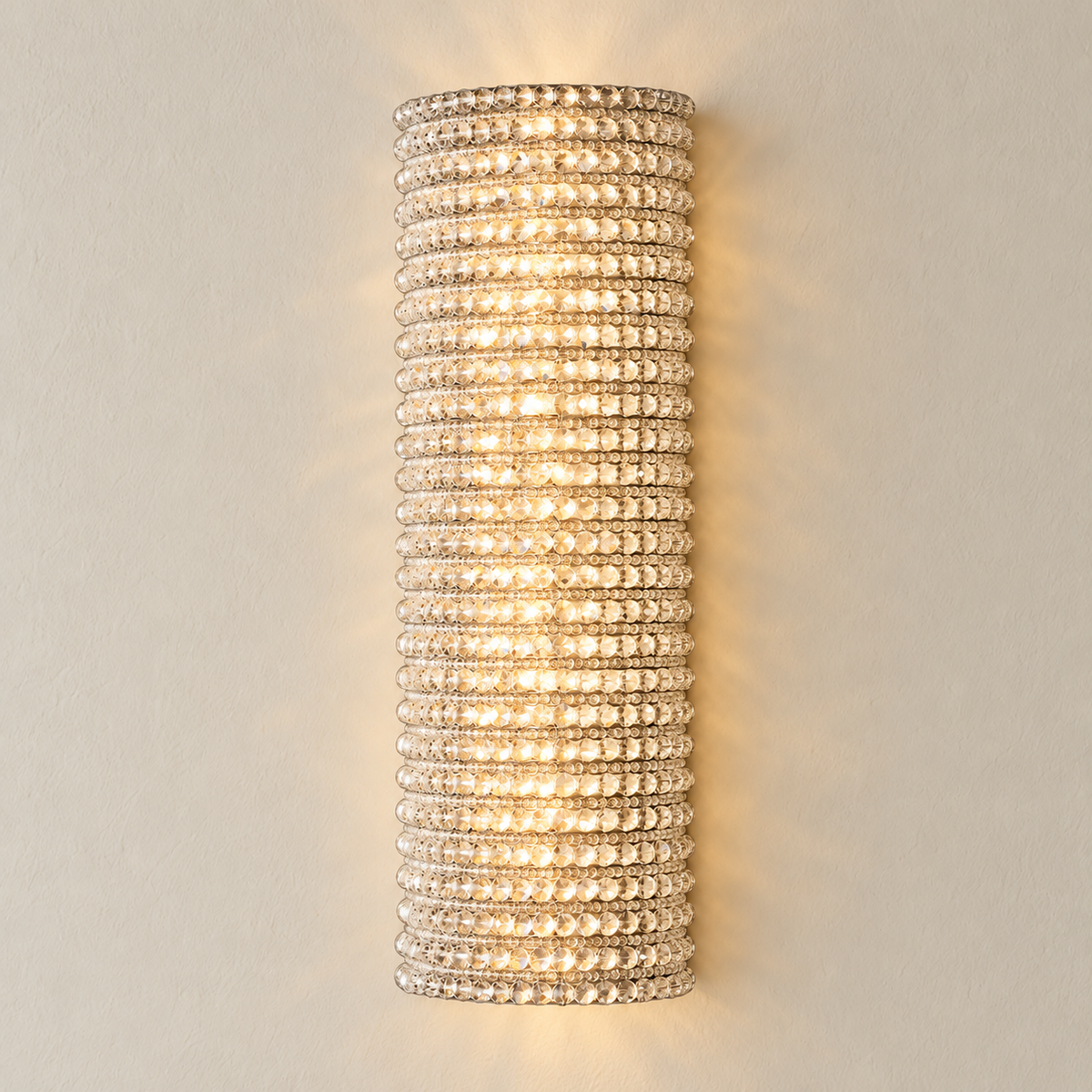 Clear crystal silver wall sconce mounted on ivory plaster, illuminated.