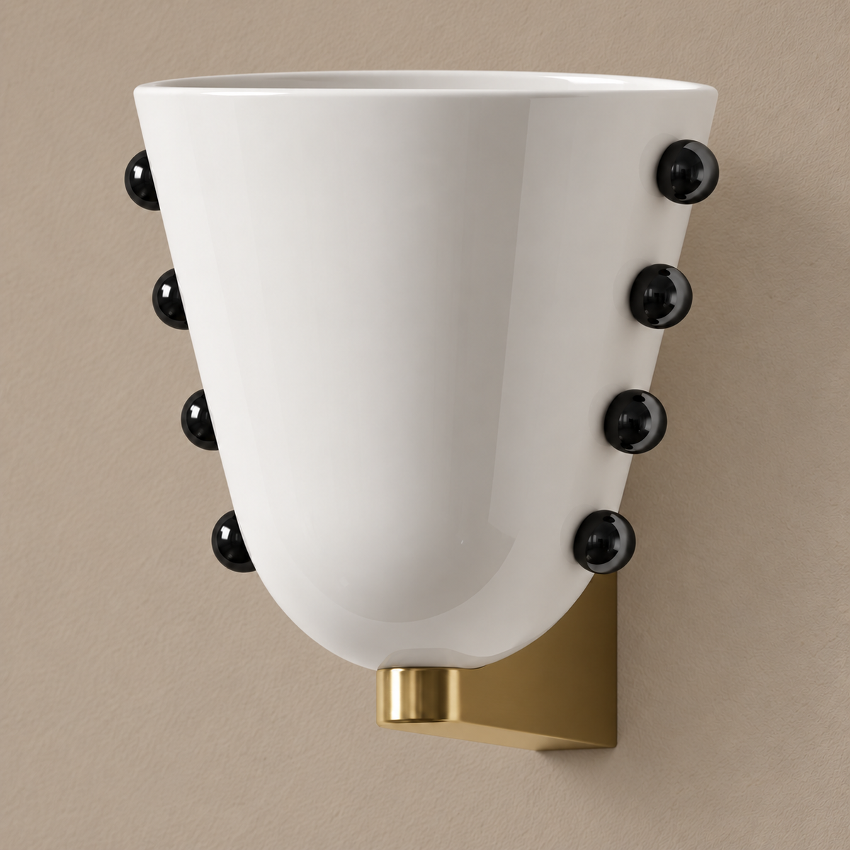 White glass wall sconce with black studs and gold brass mount, unlit on a stone-beige wall