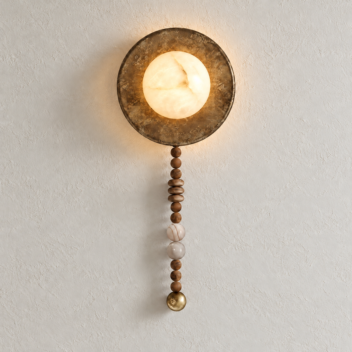 Illuminated alabaster wall sconce with a patinated round backplate and hanging wood and stone beads on warm ivory.