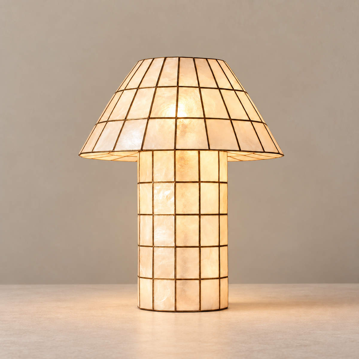 Capiz shell table lamp with a bronze grid, illuminated on a beige background
