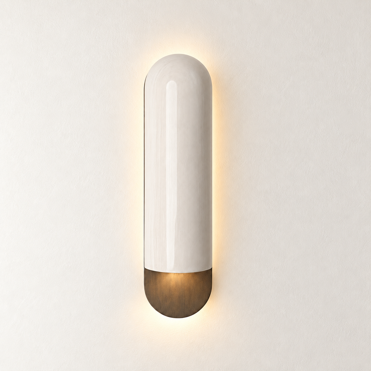 Ivory ceramic wall sconce illuminated around its bronze lower base on warm ivory.