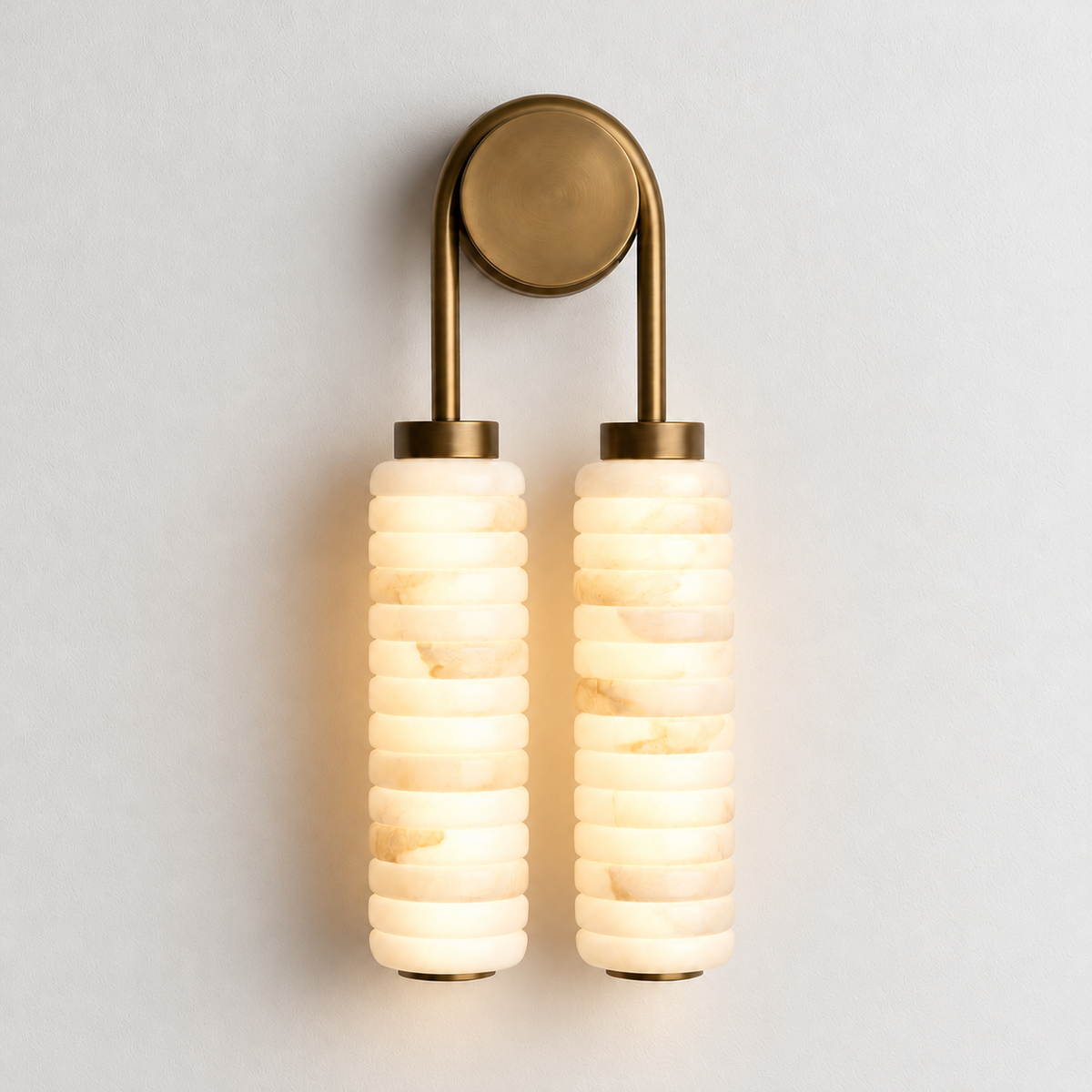 Double alabaster and brass wall sconce glowing on warm ivory.