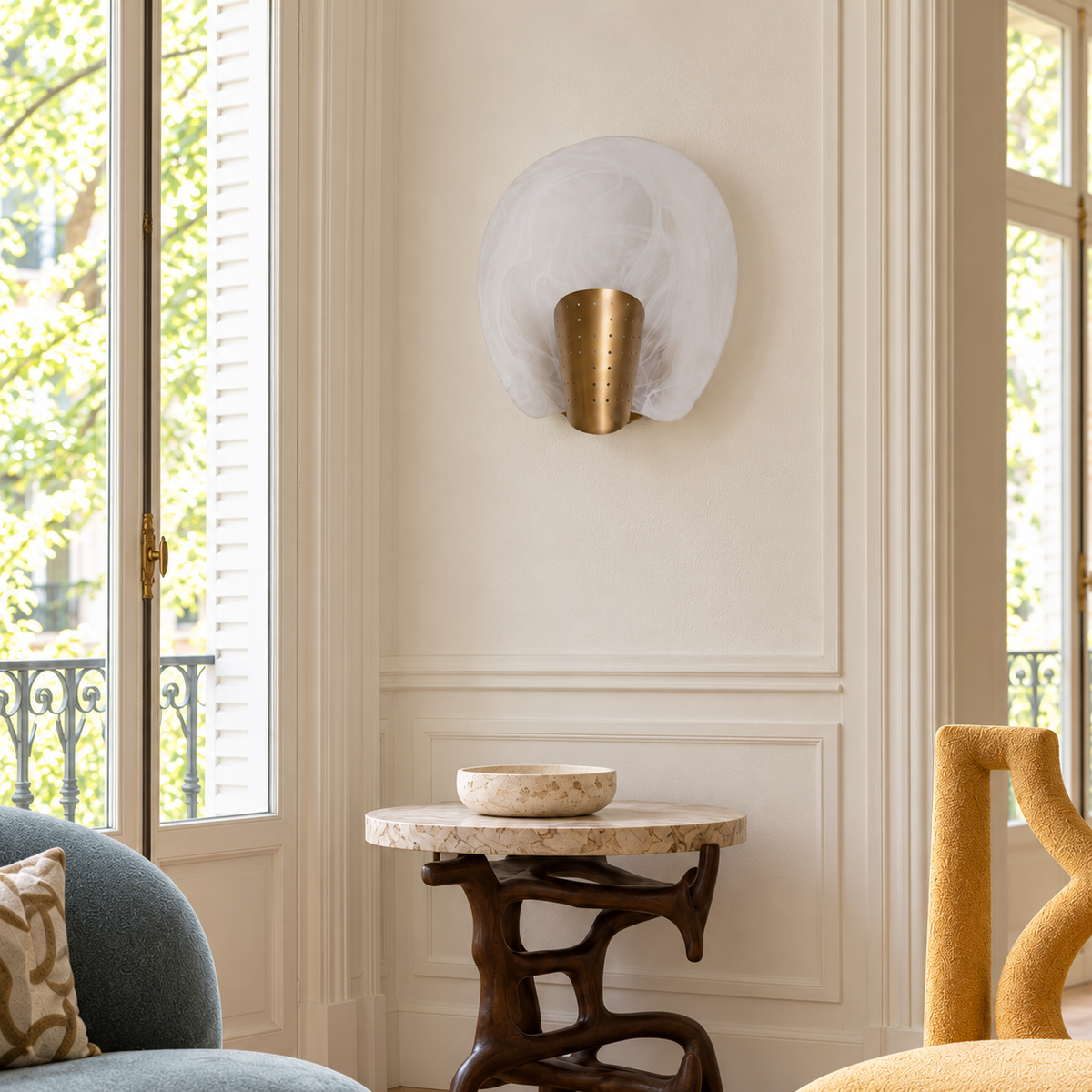 Glass and brass wall sconce above a sculptural side table between tall windows.