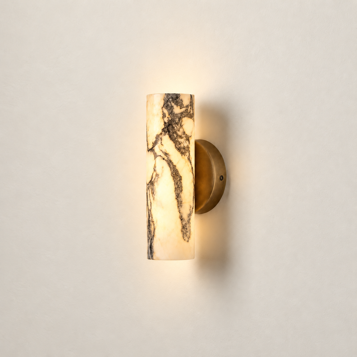 Marble cylinder wall sconce illuminated from within, with its grey veining visible against warm ivory.