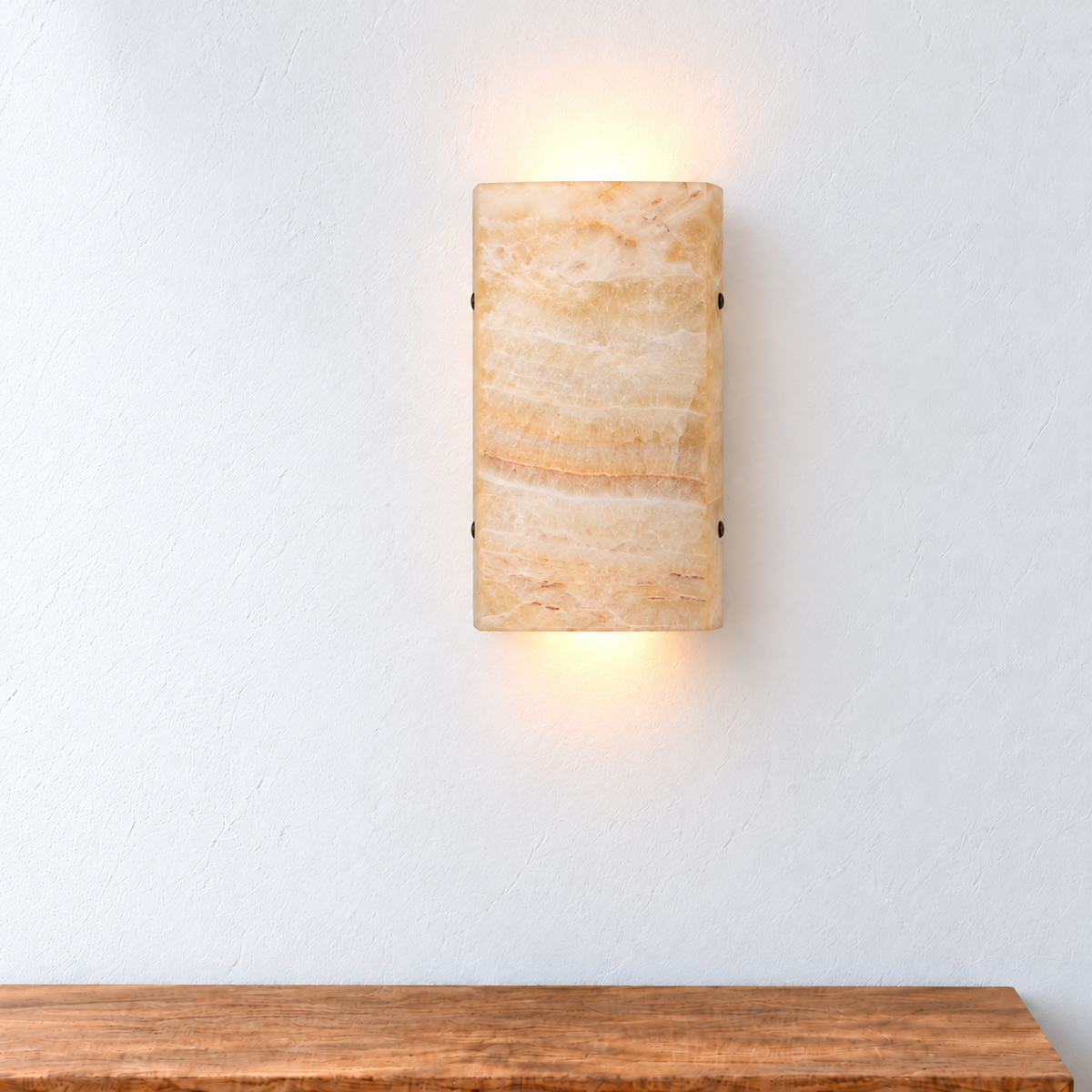 Front view of a honey onyx wall sconce mounted above an oak console in natural daylight.