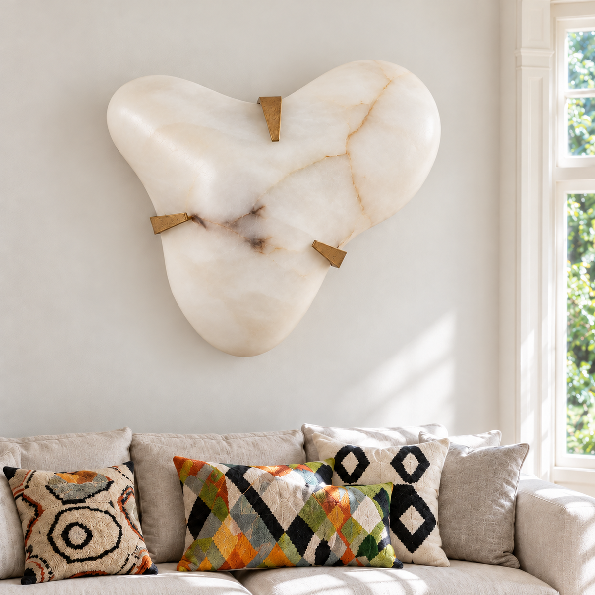Large alabaster cloud sconce mounted above a cream sofa with patterned cushions in natural daylight.