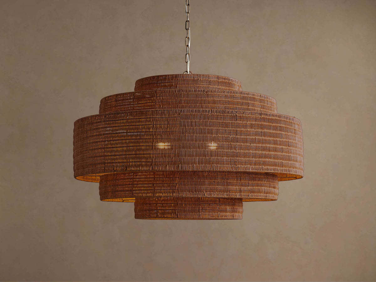 Cognac rattan chandelier lit, warm glow through the tiered woven drum