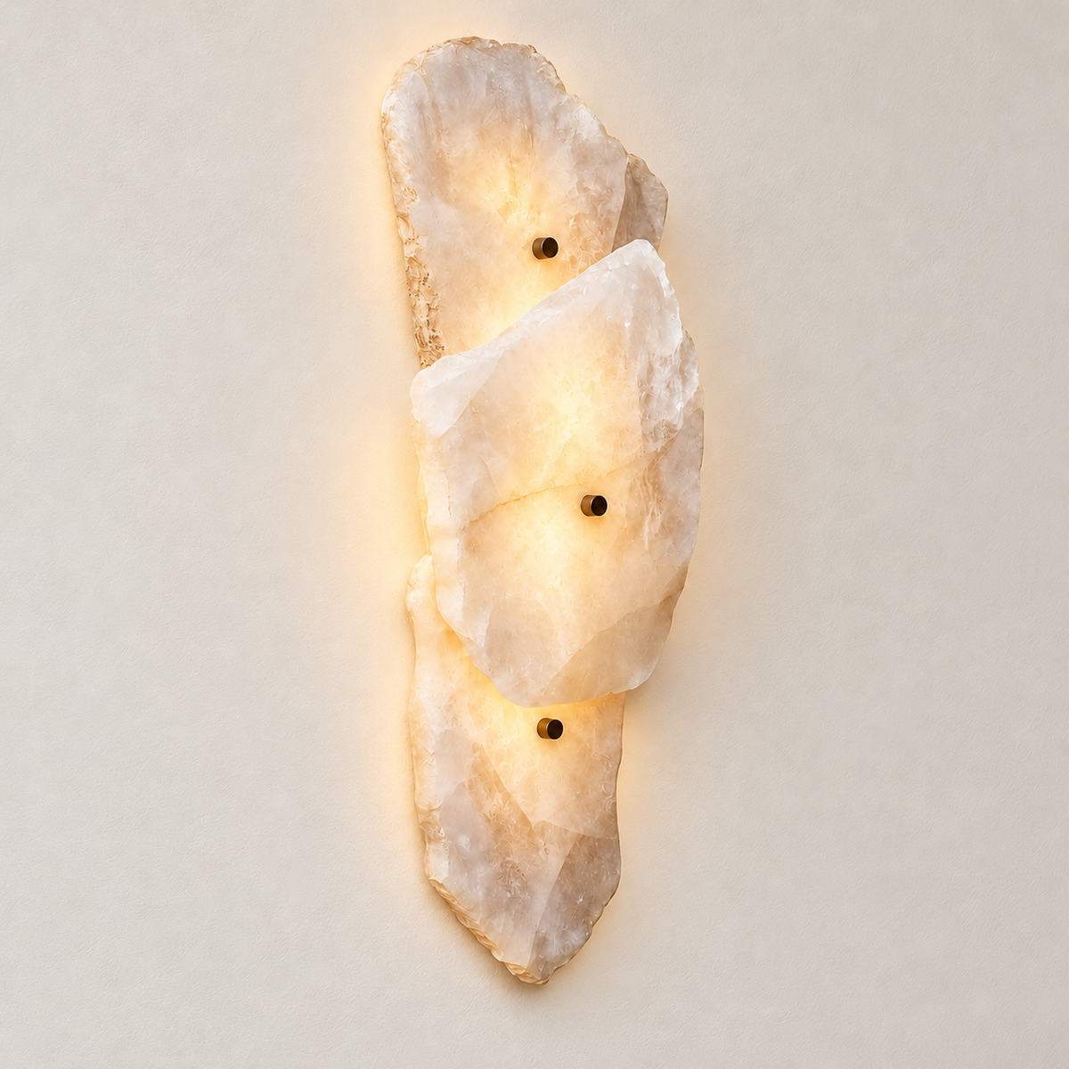 Raw stone wall sconce with three overlapping panels and dark fixing pins illuminated against the same ivory backdrop.
