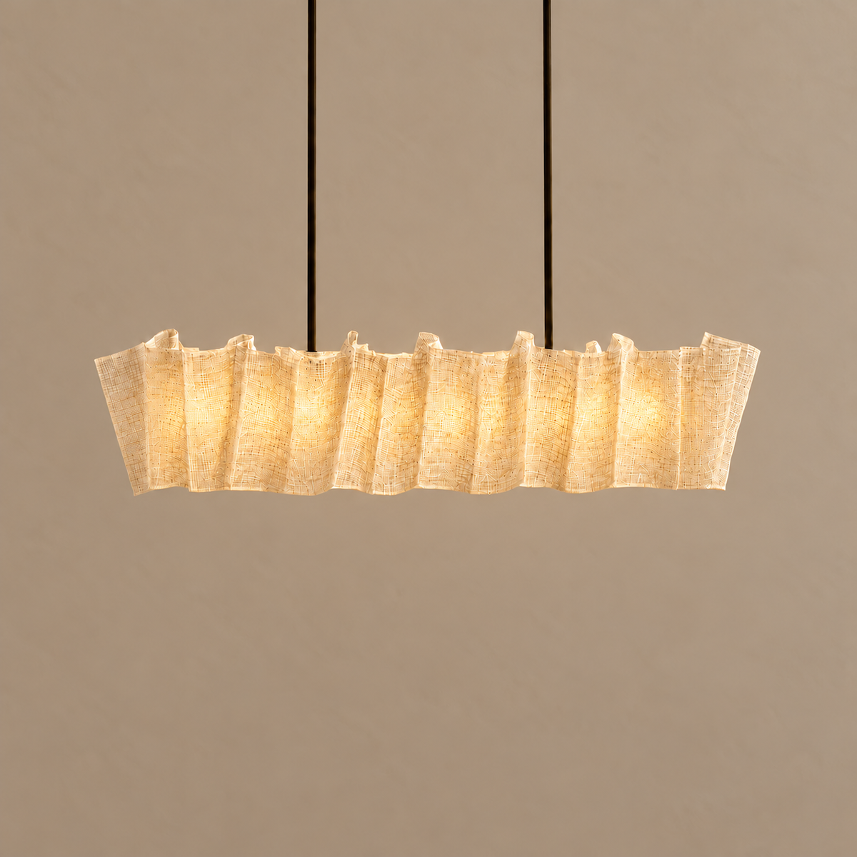 Sora linear chandelier illuminated, with warm light filtering through the fine abaca fibres.