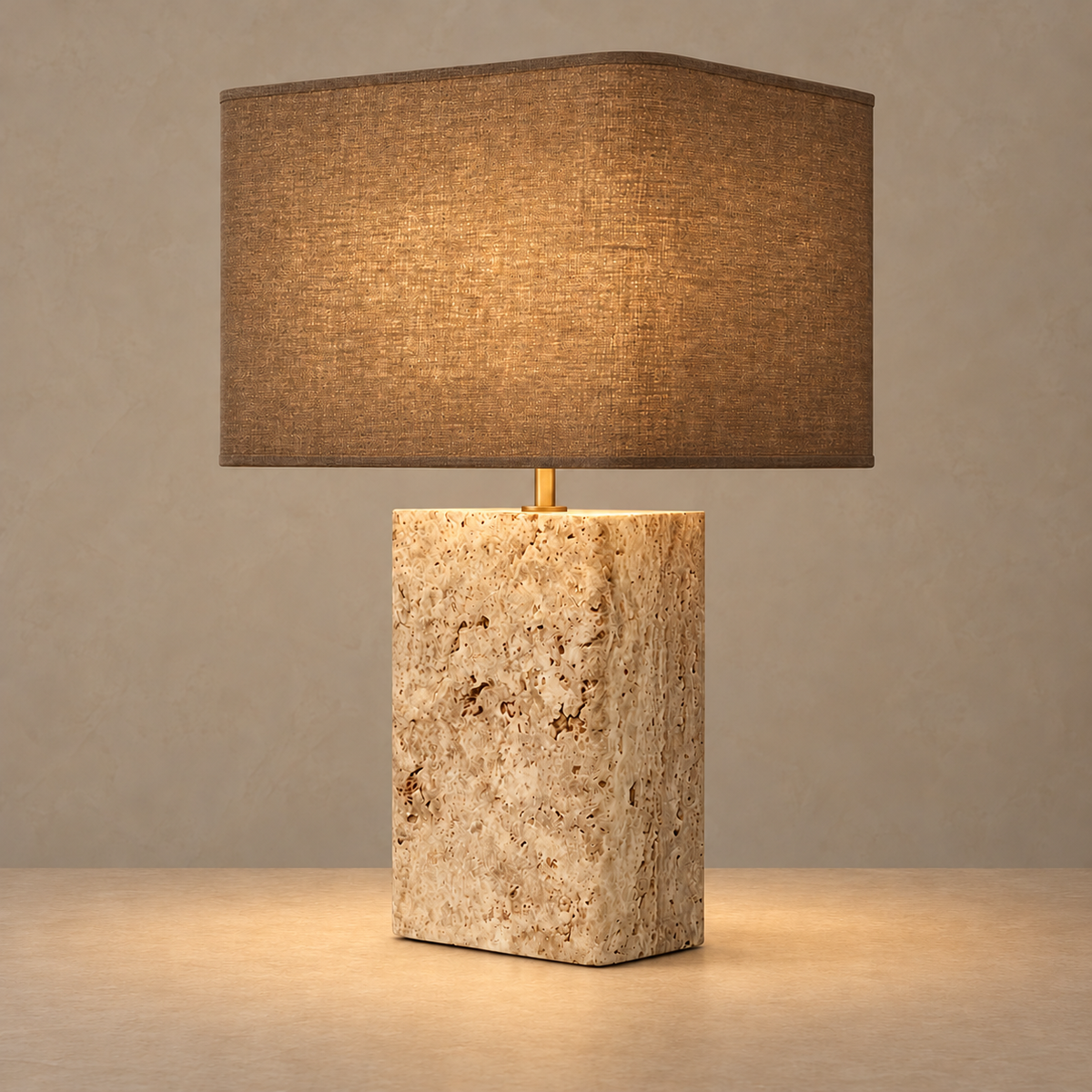 Travertine and brass table lamp illuminated through its brown woven shade.