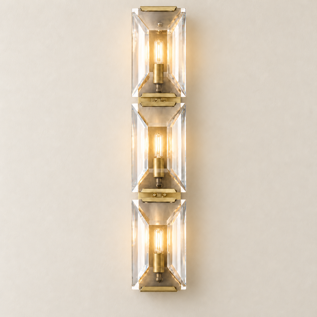 Three warm bulbs illuminate the stacked crystal panels of the brass wall sconce.
