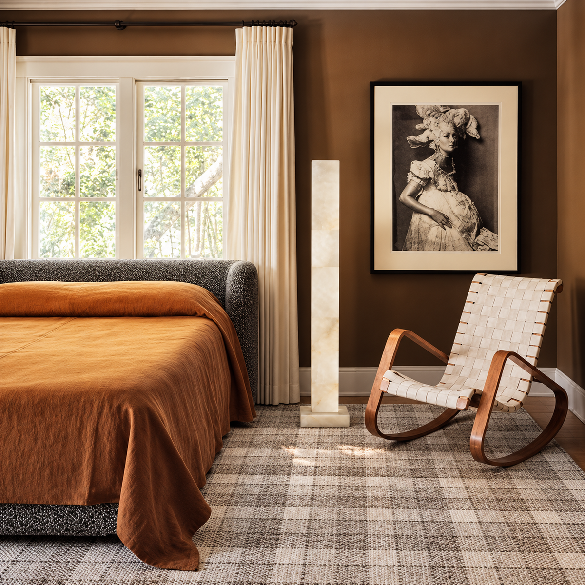 Large alabaster column lamp beside a bentwood rocking chair in a brown bedroom.
