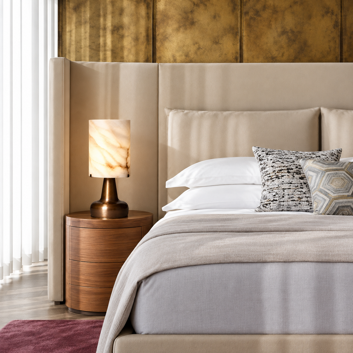 Alabaster cylinder table lamp on a walnut bedside table beside a cream upholstered bed.
