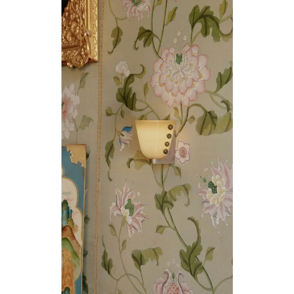 Studded cone wall sconce lit on botanical wallpaper