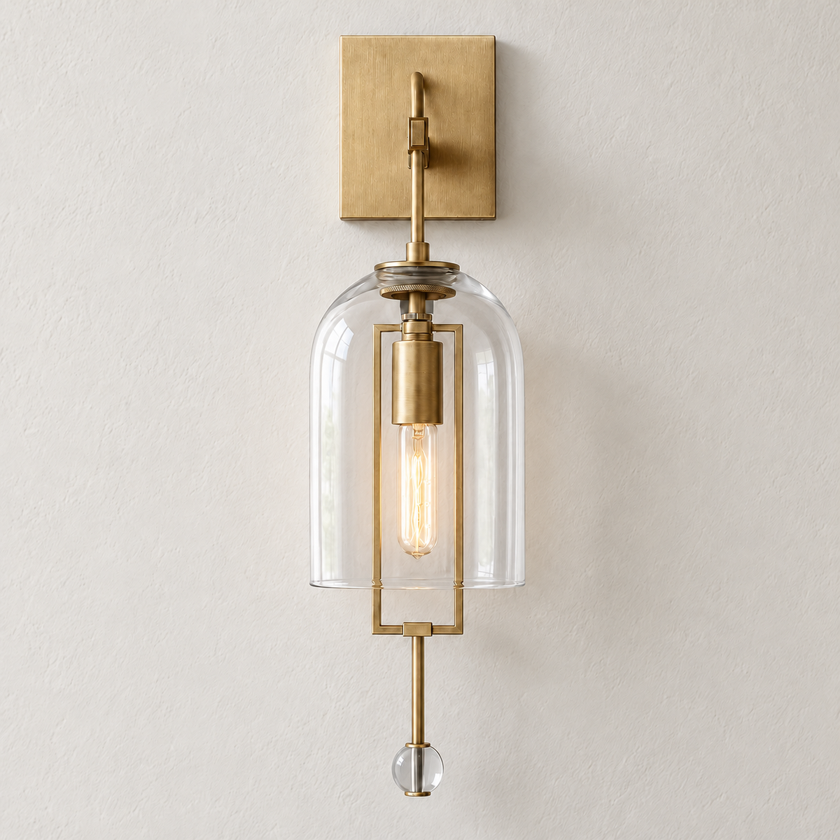 Brass wall sconce with an open-bottom glass bell and crystal finial, illuminated on ivory plaster.