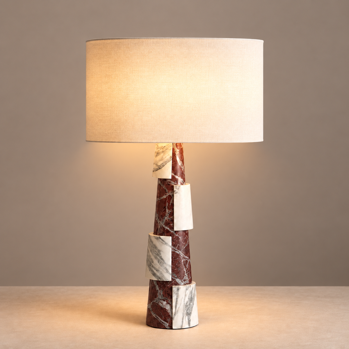 Burgundy and white marble table lamp illuminated beneath its natural linen drum shade.