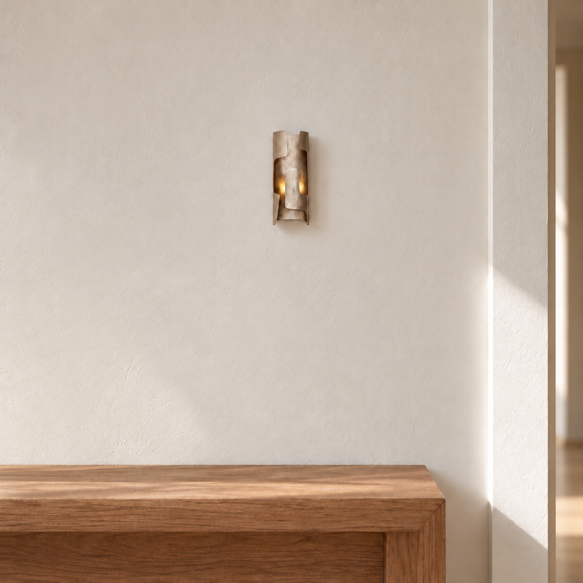 Champagne bronze wall sconce mounted above a clear oak console on an ivory entryway wall.