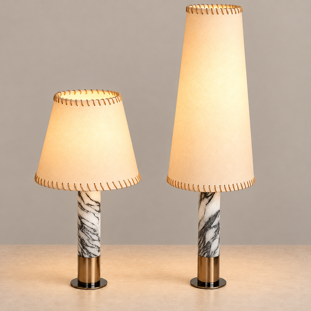 Short and tall parchment table lamps with veined marble columns, illuminated on a beige background