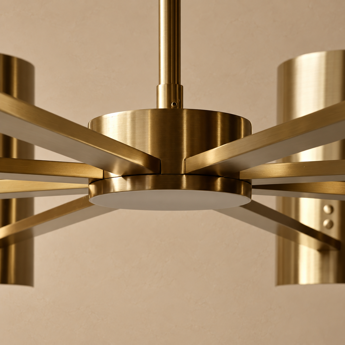 Close-up of the CLDVY73 chandelier’s brass hub, suspension collar and radial arms against a beige background.