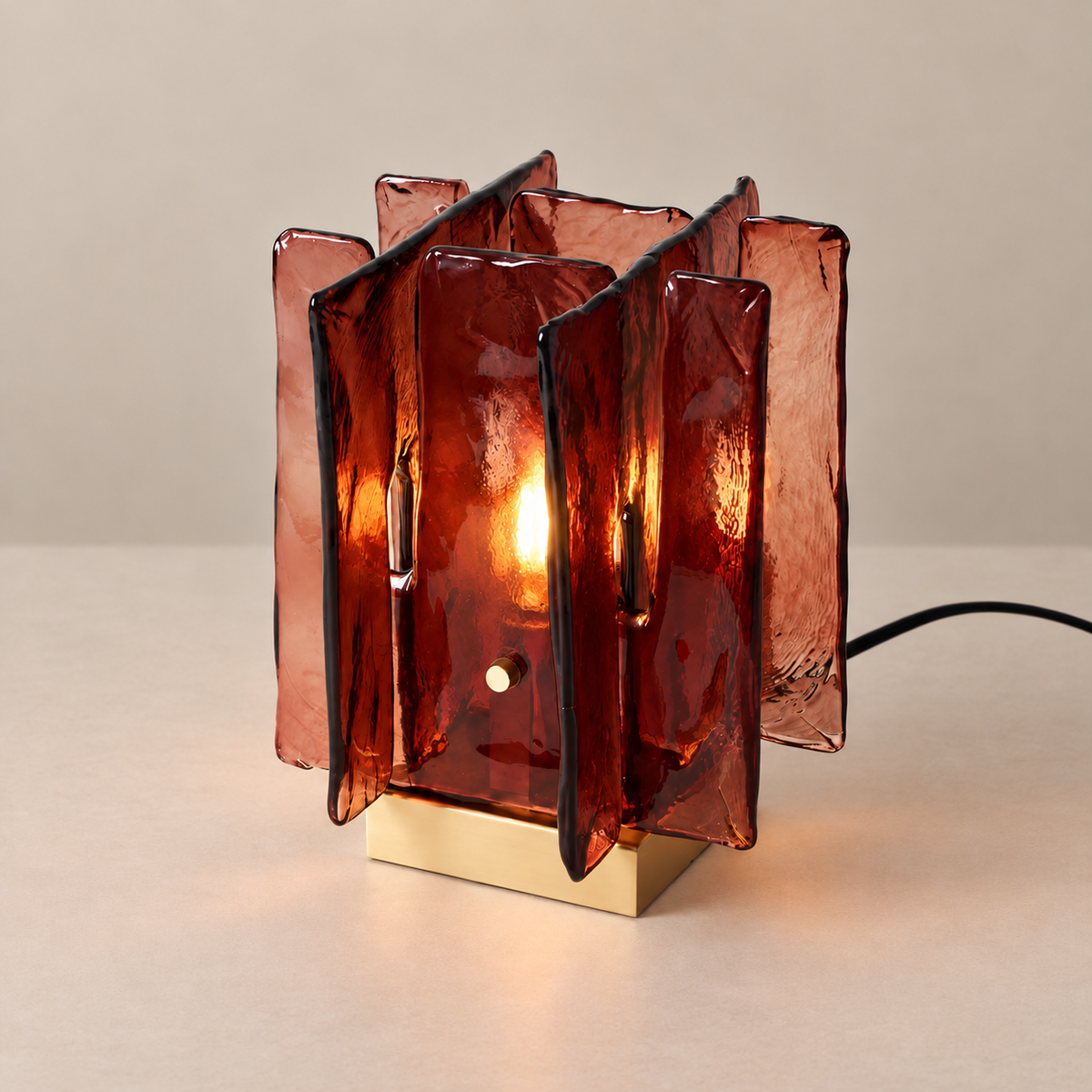 Burgundy glass Blades table lamp illuminated on a beige background.