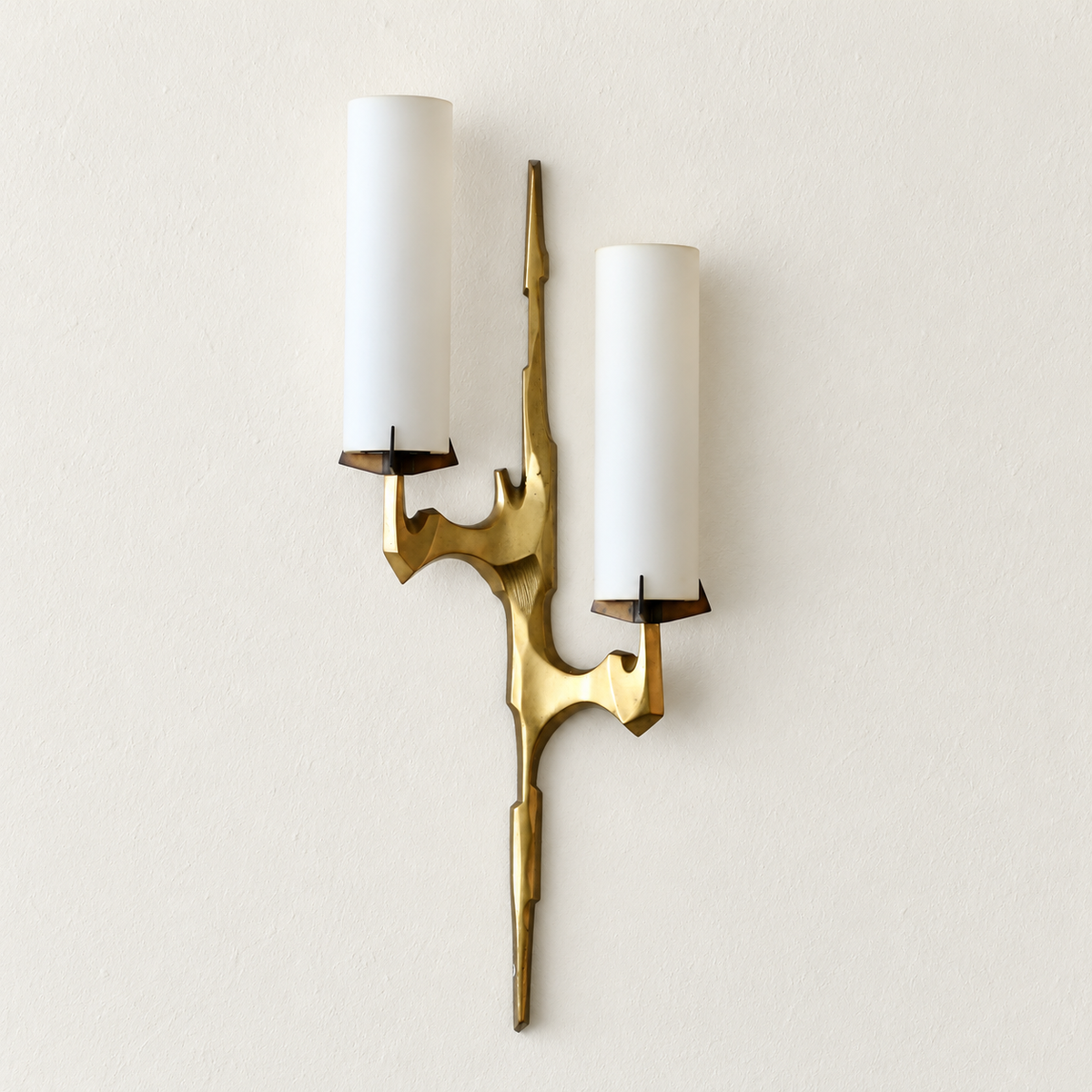Sculptural brass sconce with two staggered opal glass shades unlit against warm ivory plaster.
