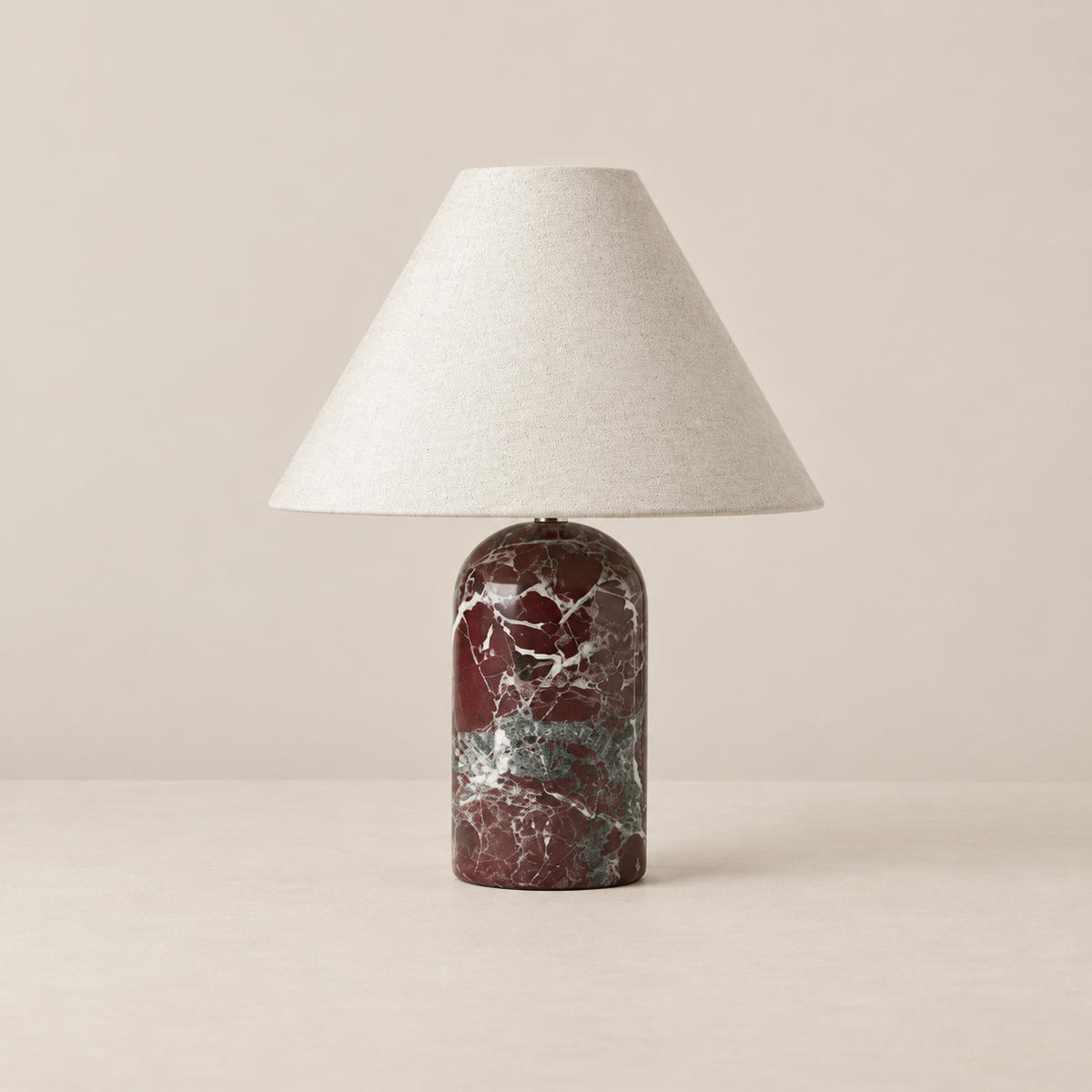Red marble table lamp with ivory linen shade, switched off on a beige background.