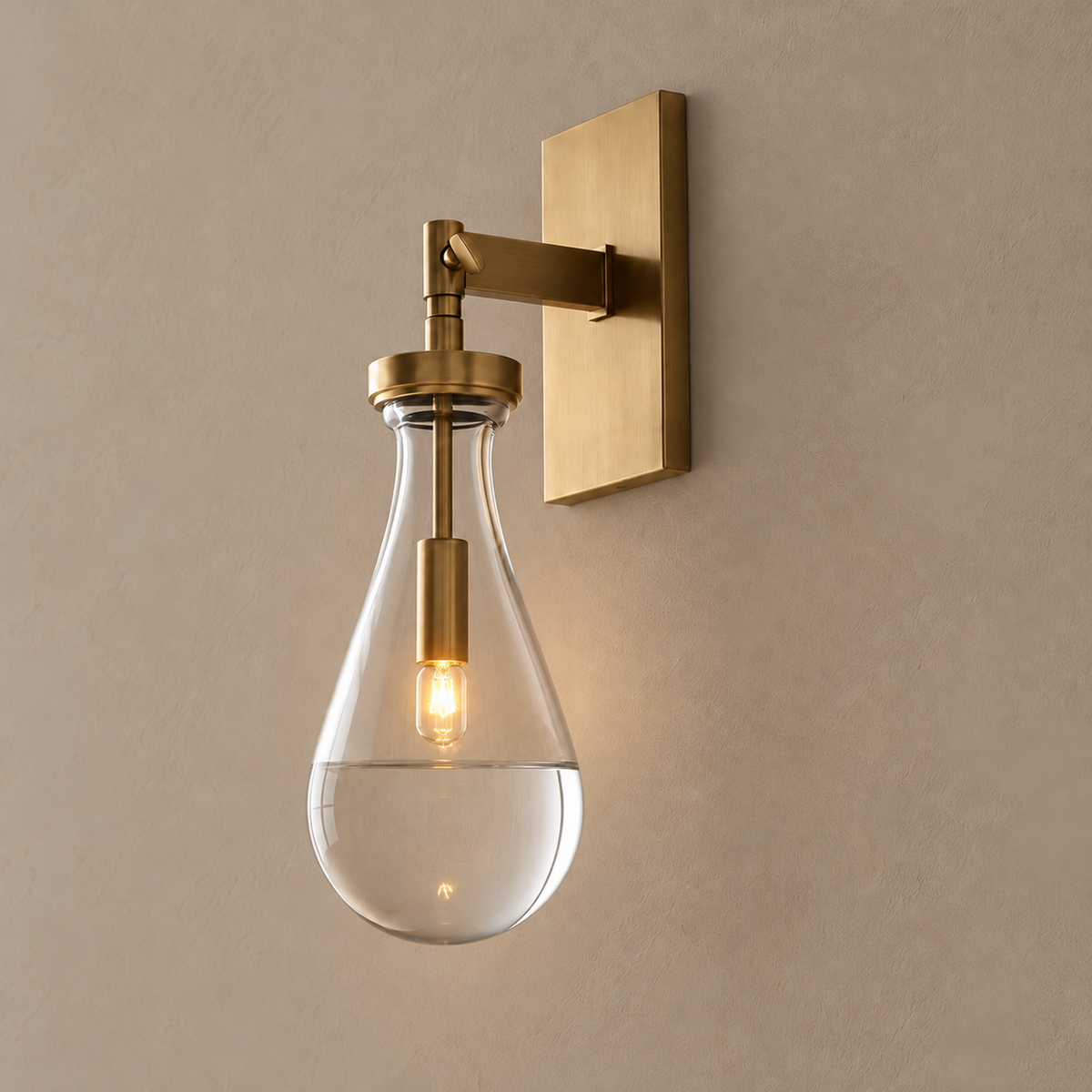 Raindrop glass wall sconce illuminated, with a brass arm and clear teardrop shade.