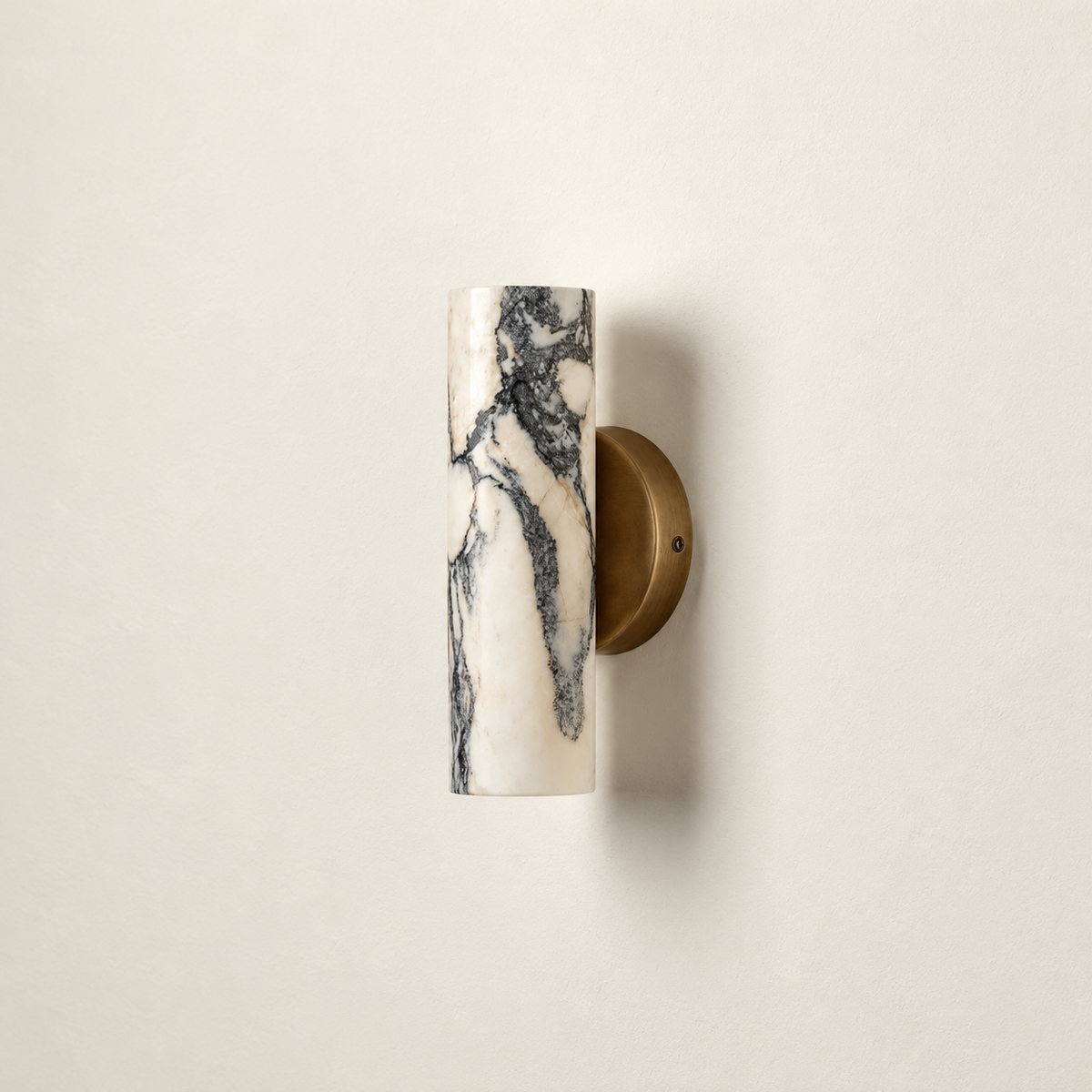 Unlit white marble cylinder wall sconce with dark veining and a round brass backplate.