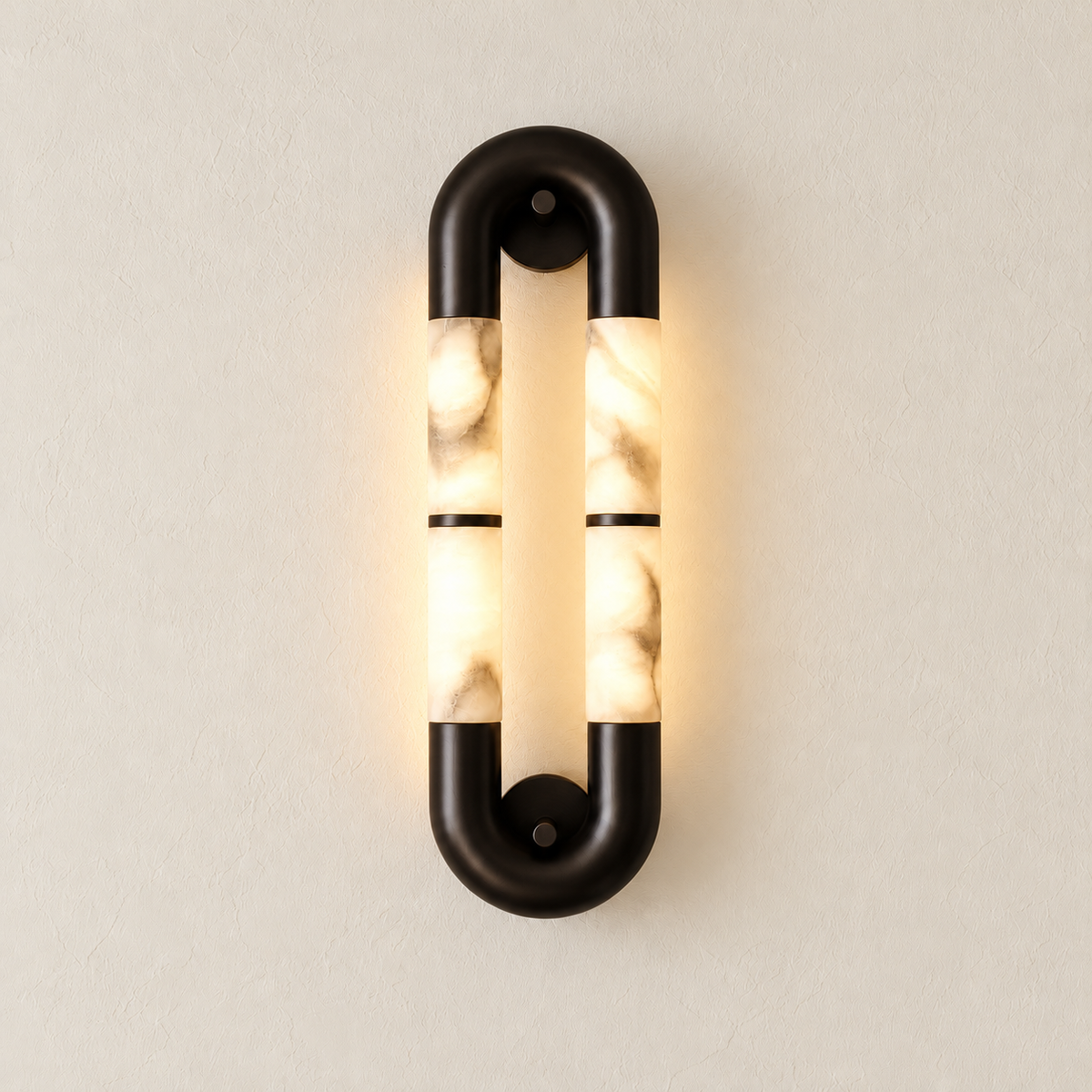 Elongated alabaster oval wall sconce with black metal connectors illuminated against the same warm ivory backdrop.