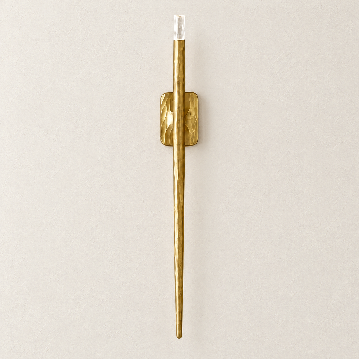 Front view of the long textured brass wall sconce, switched off on ivory plaster.