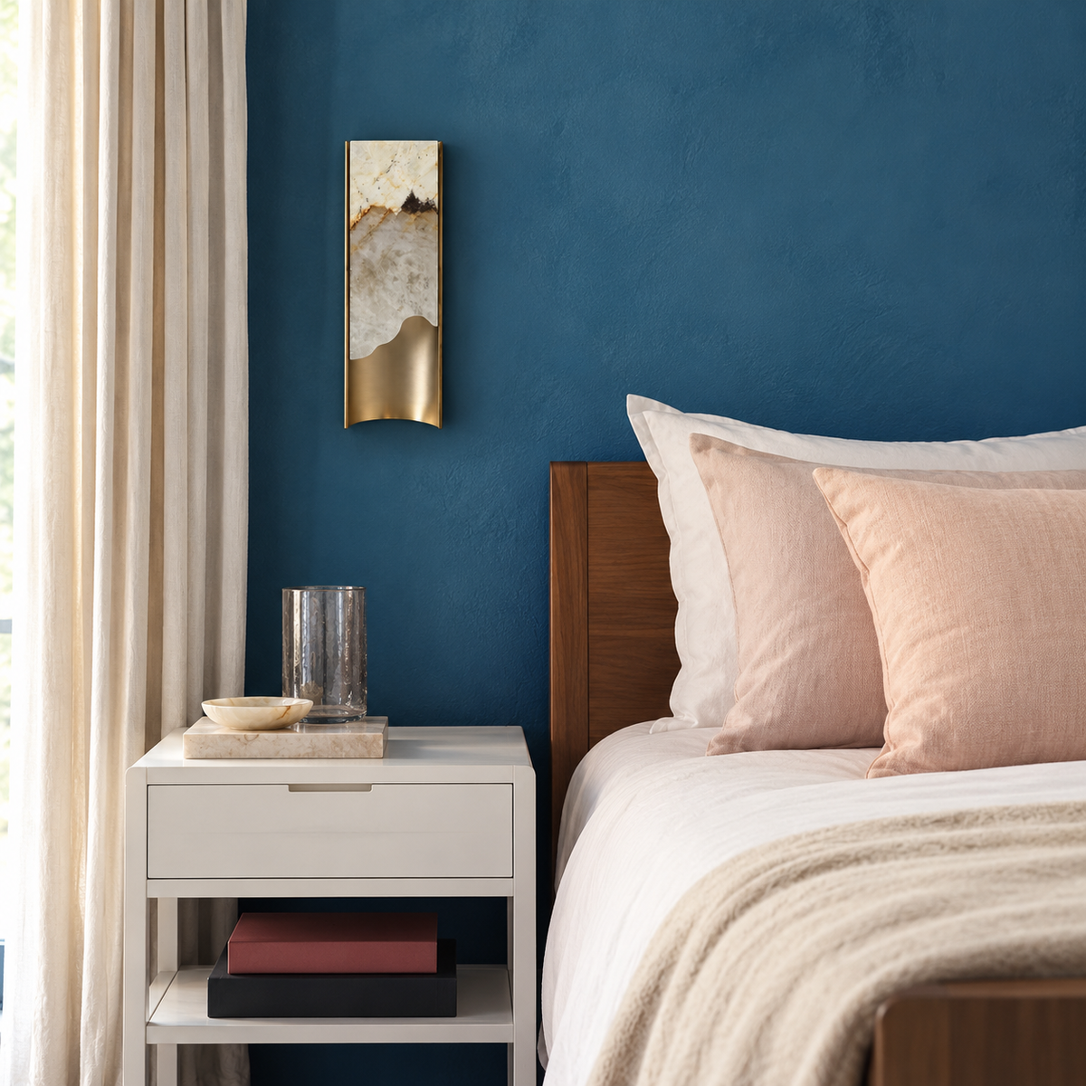 Small onyx and brass wall sconce beside a bed against a blue wall.