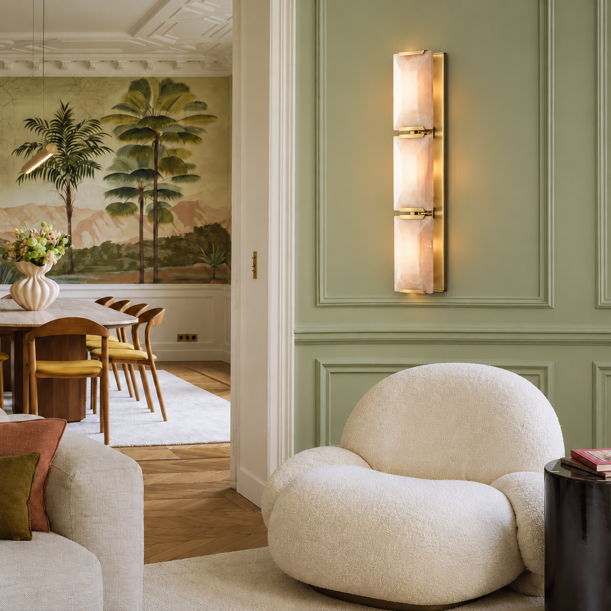 Triple calcite wall sconce with brass hardware installed on a sage wall beside a cream armchair.