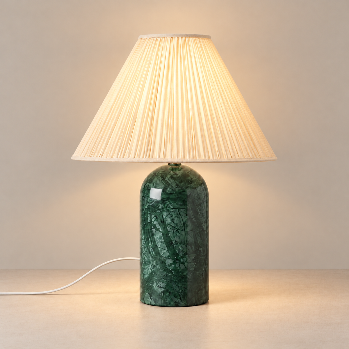 Green marble table lamp with its cream pleated linen shade illuminated.