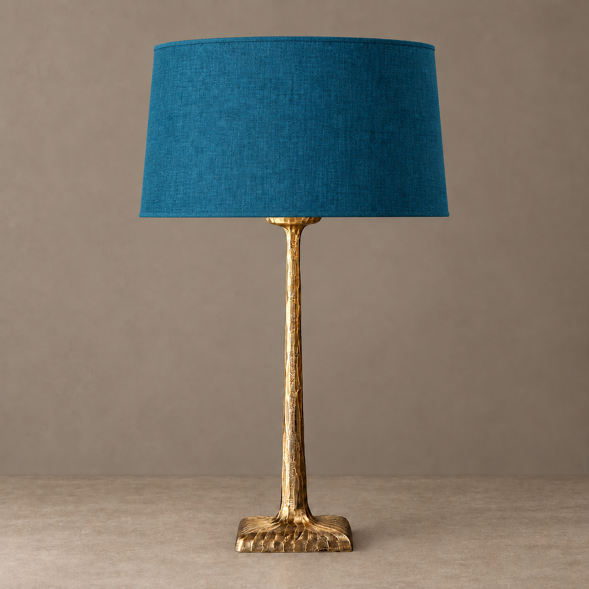 Hammered brass table lamp with a petrol blue tapered fabric shade, unlit.