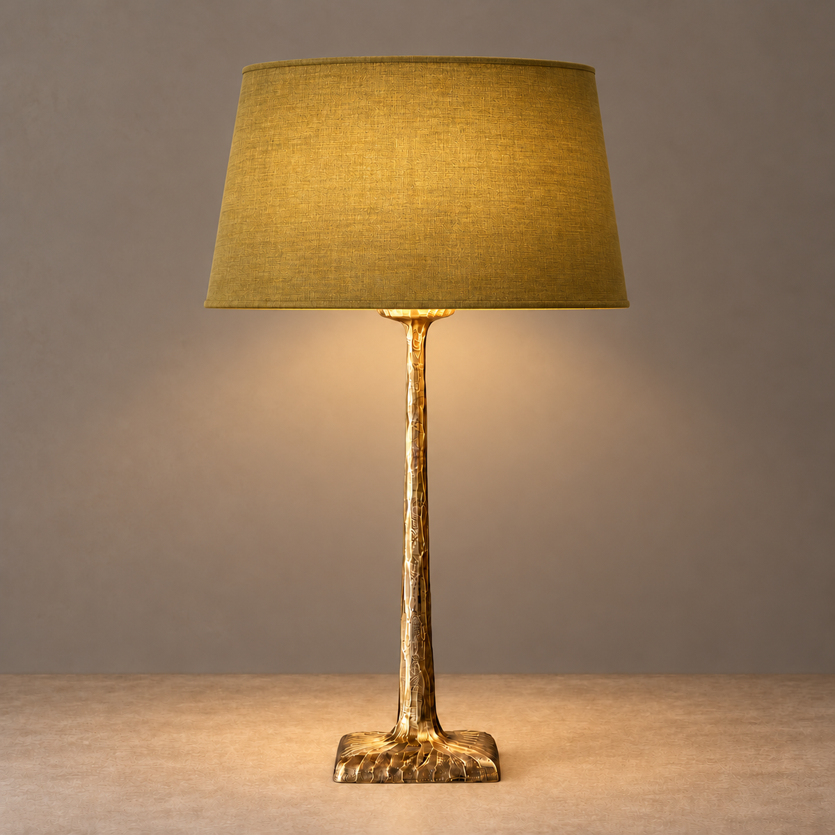 Hammered brass table lamp illuminated beneath its olive tapered fabric shade.